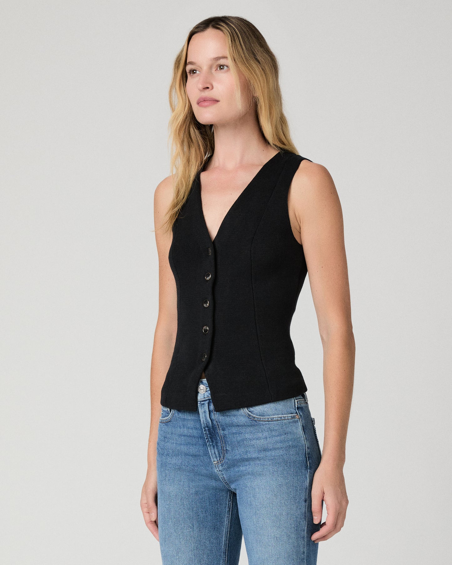 Women wearing a black vest top and blue jeans against a white background