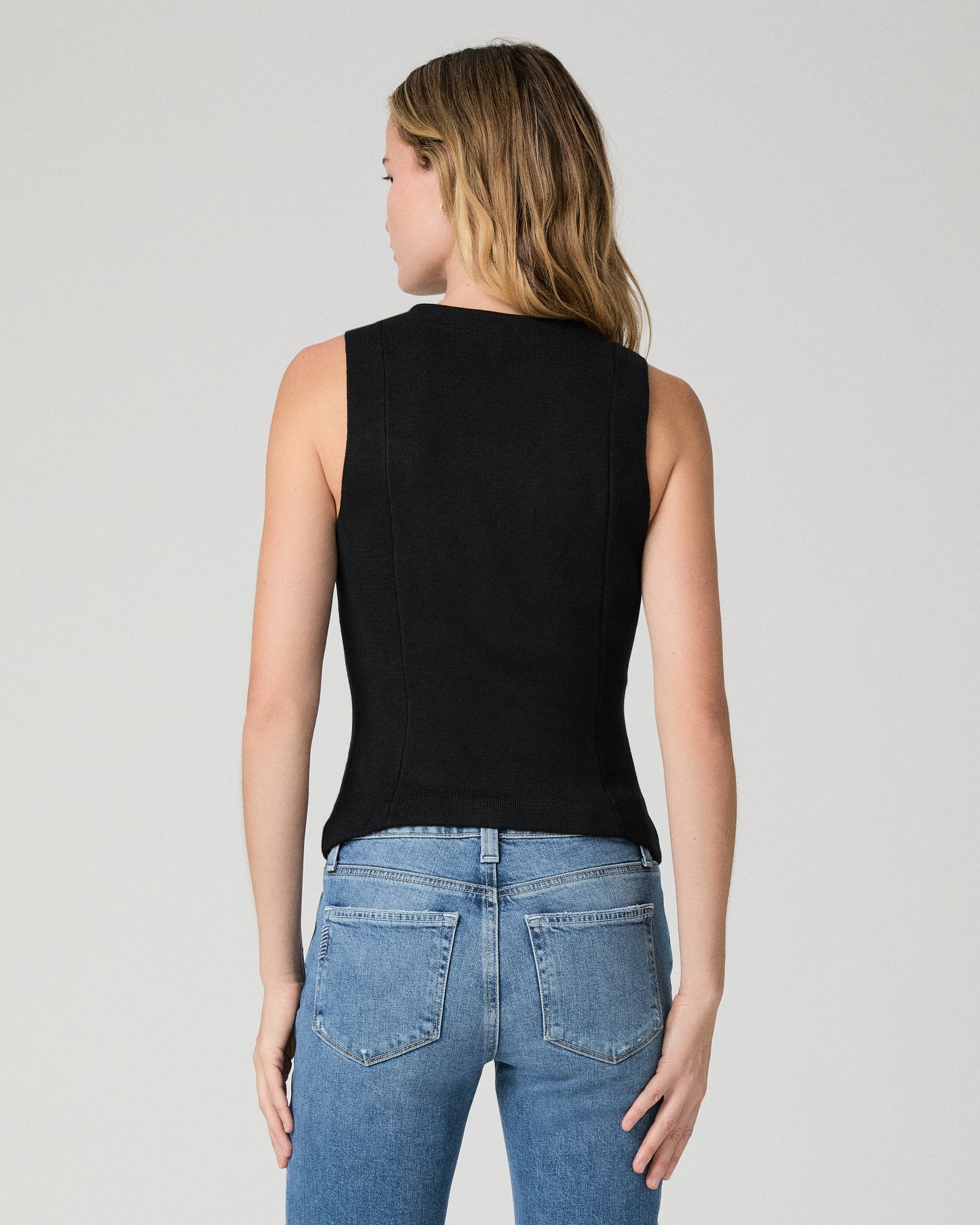 Women wearing a black vest top and blue jeans against a white background