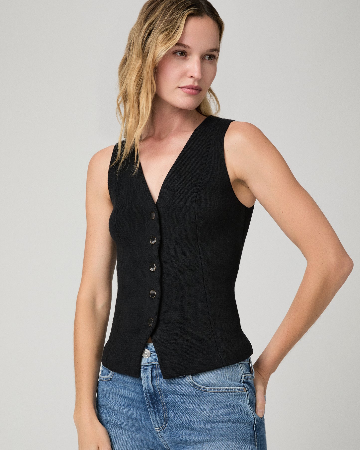 Women wearing a black vest top and blue jeans against a white background