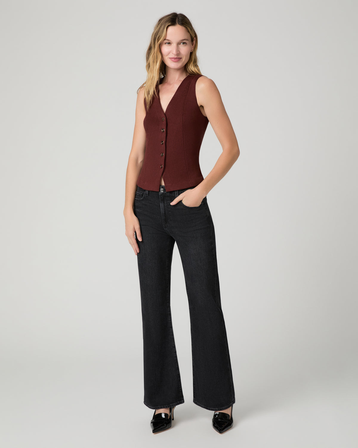 Women wearing a burgundy vest top paired with black jeans and black heels  against a white background