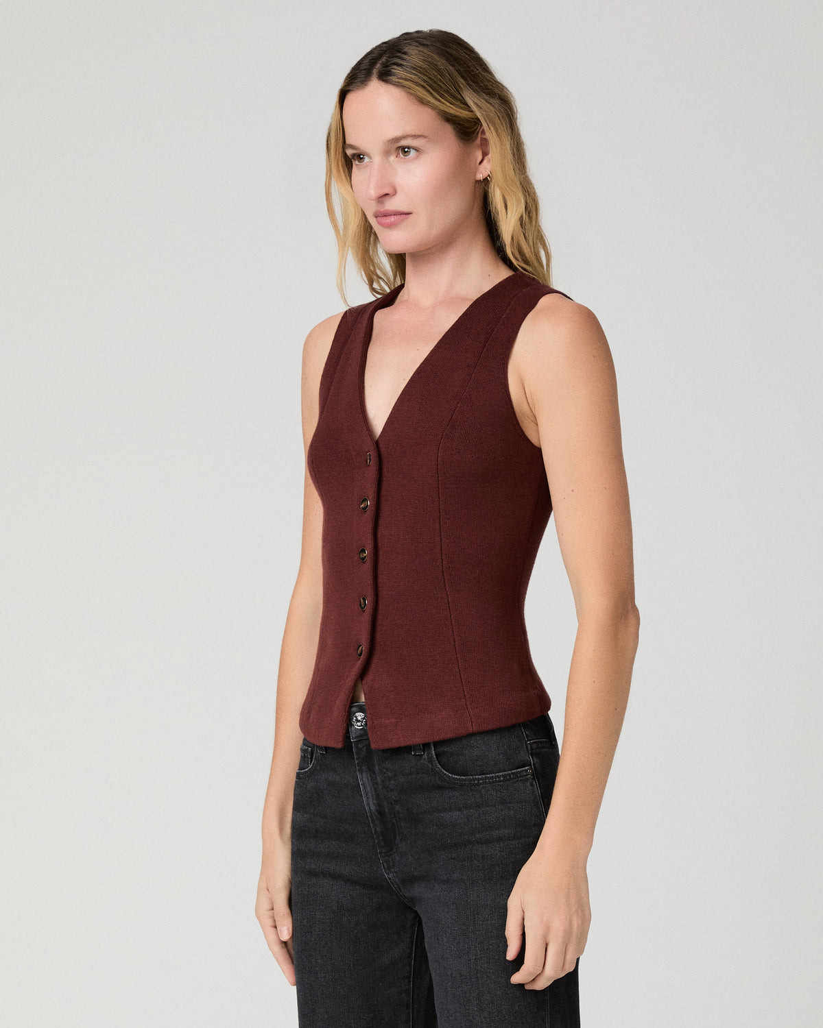 Women wearing a burgundy vest top paired with black jeans against a white background