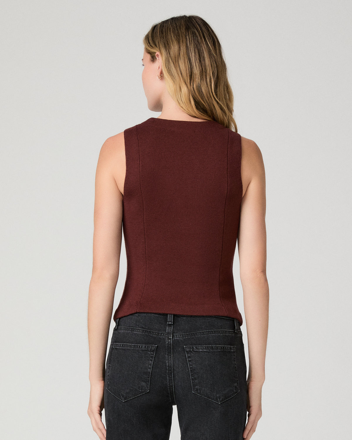 Women wearing a burgundy vest top paired with black jeans against a white background