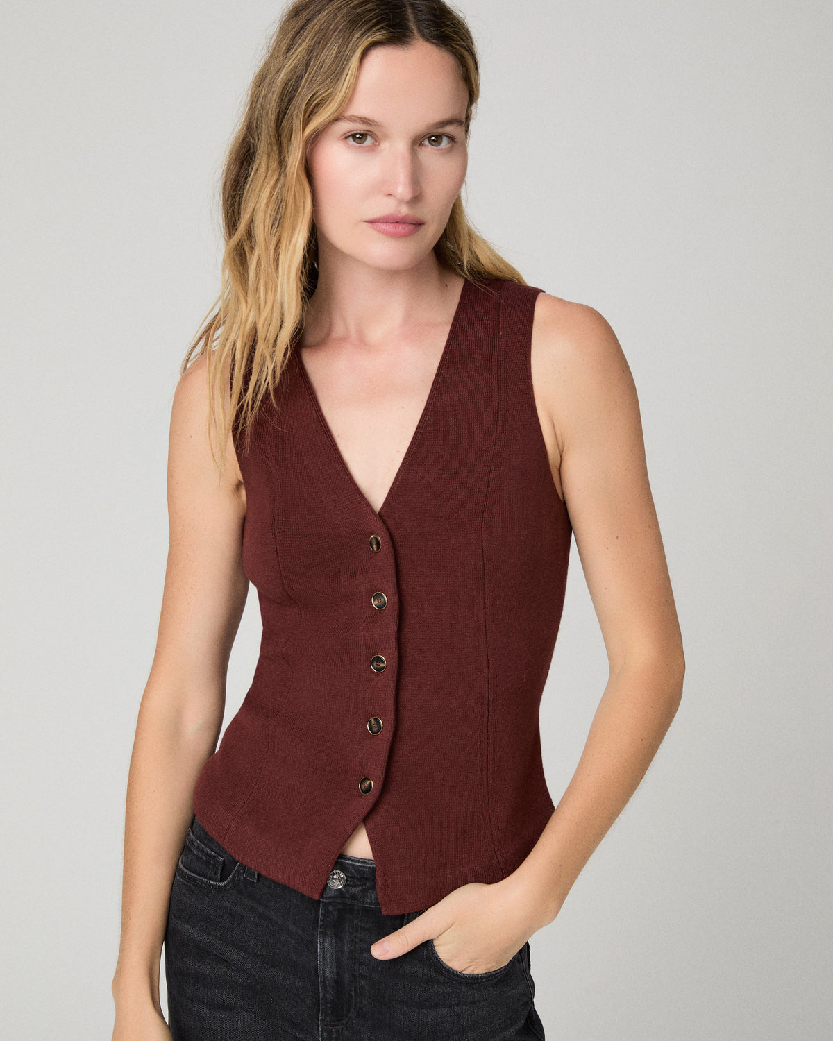 Women wearing a burgundy vest top paired with black jeans against a white background