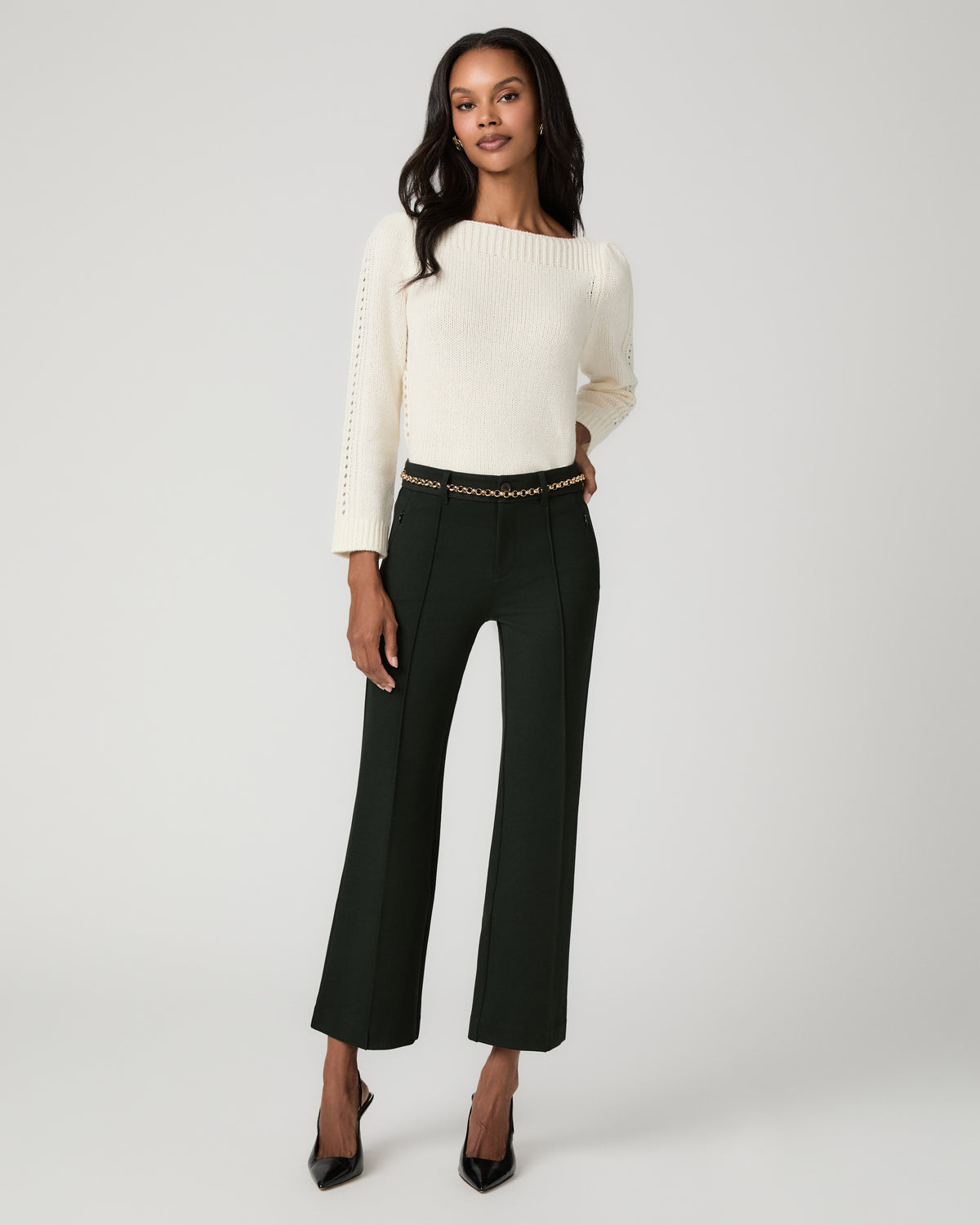 Full-length front view of a woman wearing an ivory knit sweater and dark spruce green cropped flare trousers with a tonal striped waistband, black pointed-toe pumps.