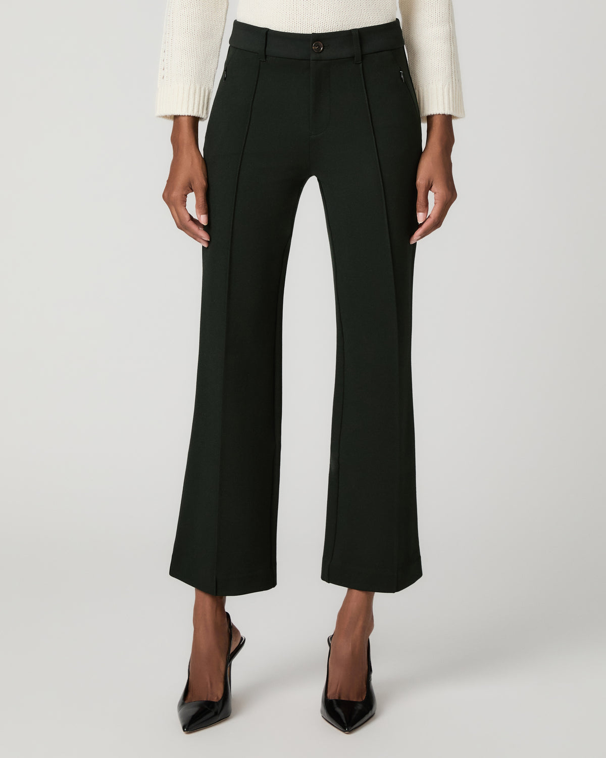 Close-up front view of dark spruce green cropped flare trousers with pintuck front seams, paired with black ankle-strap heels.