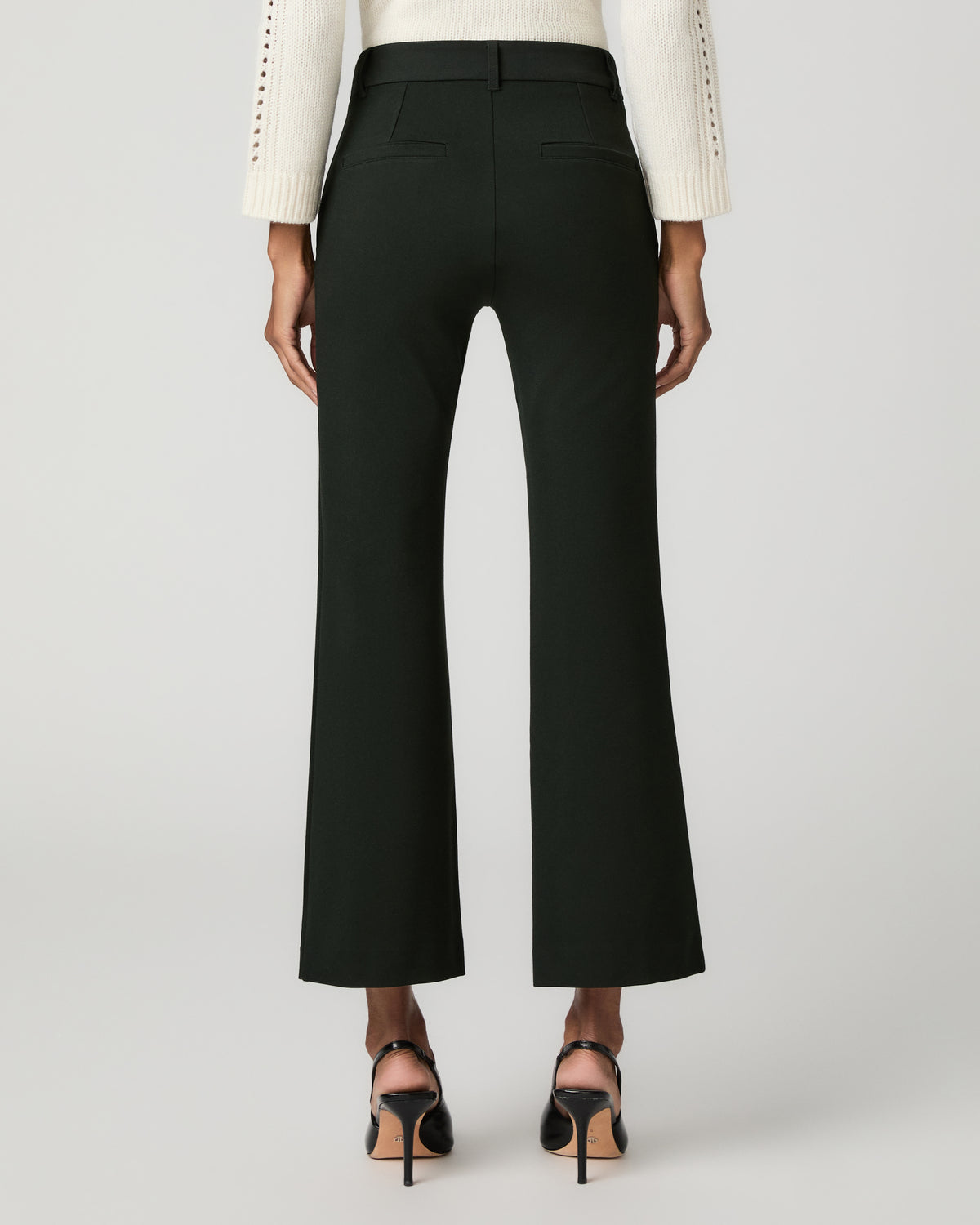Close-up front view of a woman's hand in the side pocket of dark spruce green cropped flare trousers with a button waistband.