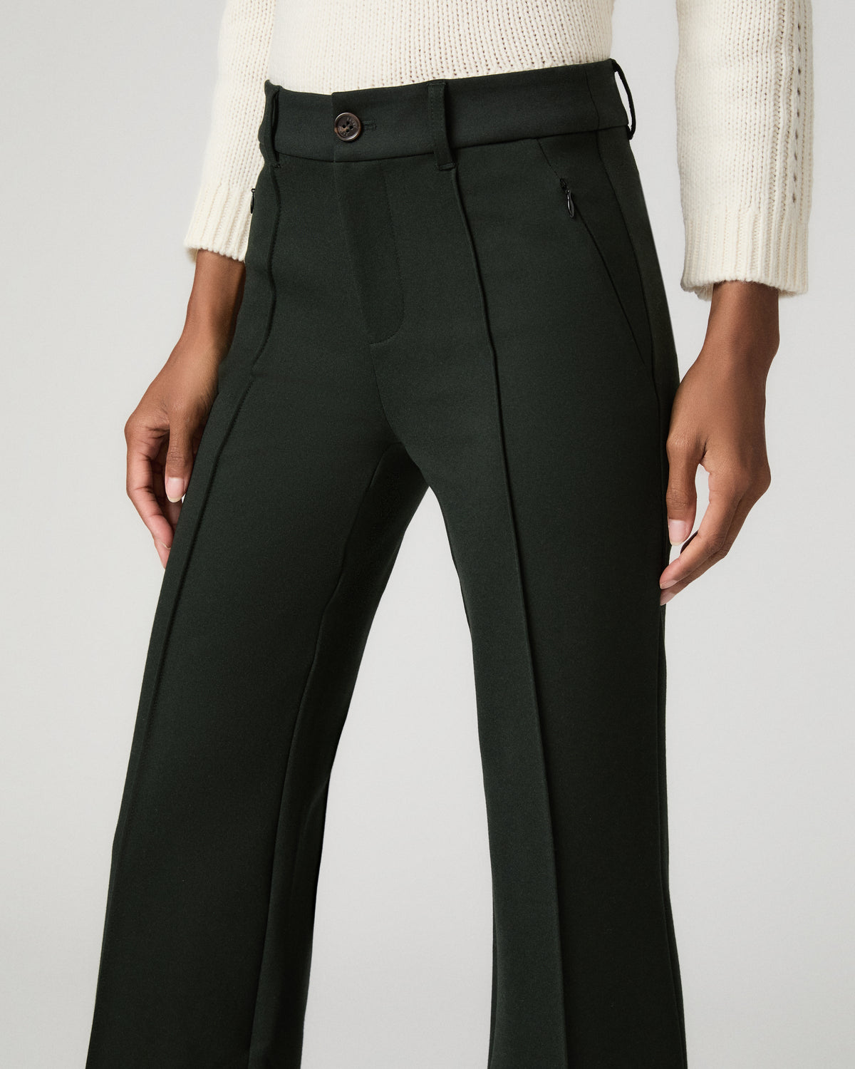 Back view close-up of dark spruce green cropped flare trousers showing the back yoke seaming, paired with black ankle-strap heels.