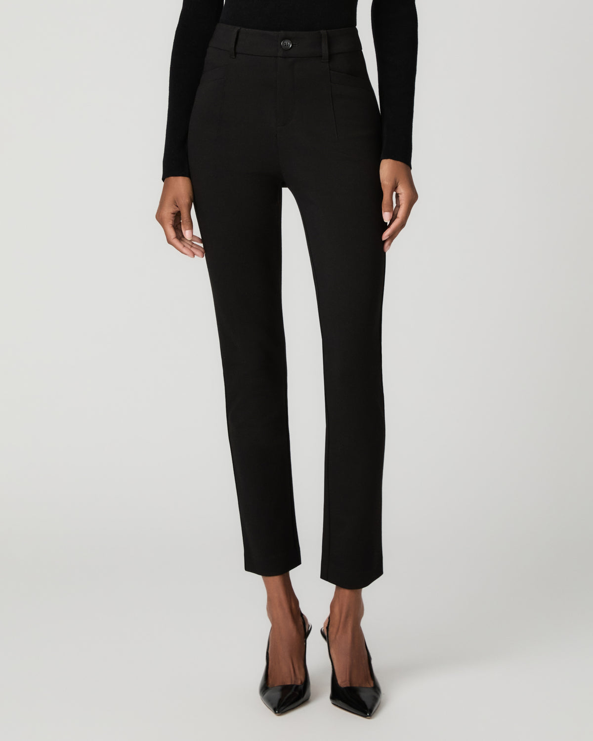 Close-up front view of black slim tapered ankle-length trousers with a fitted waistband, paired with black pointed-toe pumps.