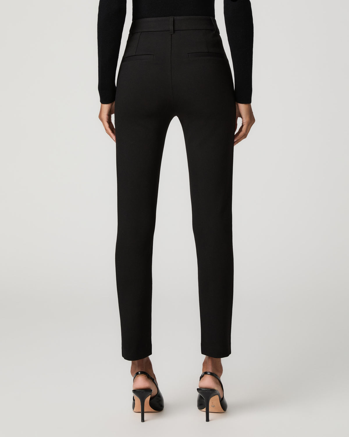Back view of a woman wearing black slim tapered ankle-length trousers with a fitted waistband and welt back pockets.