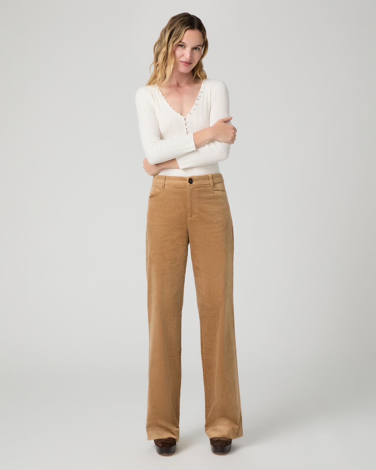 A woman modeling a white long-sleeve knit top with lace trim and tan wide-leg corduroy pants against a light gray studio background.