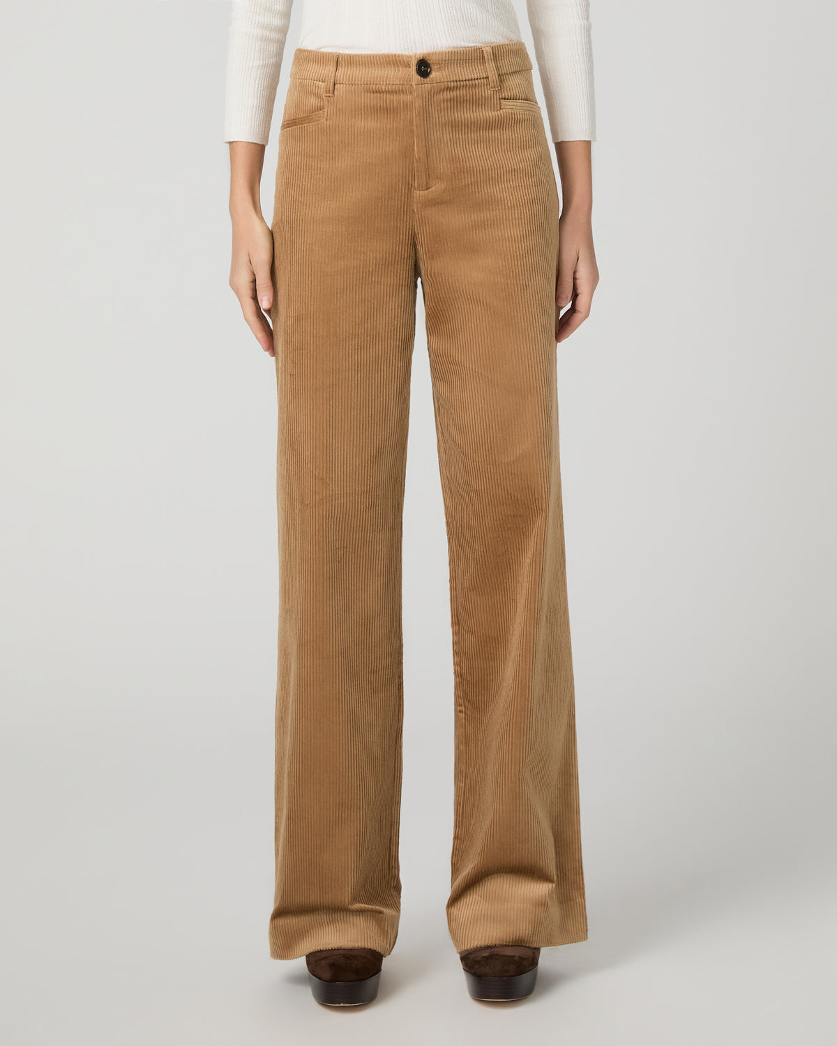 A woman modeling a white long-sleeve knit top with lace trim and tan wide-leg corduroy pants against a light gray studio background.
