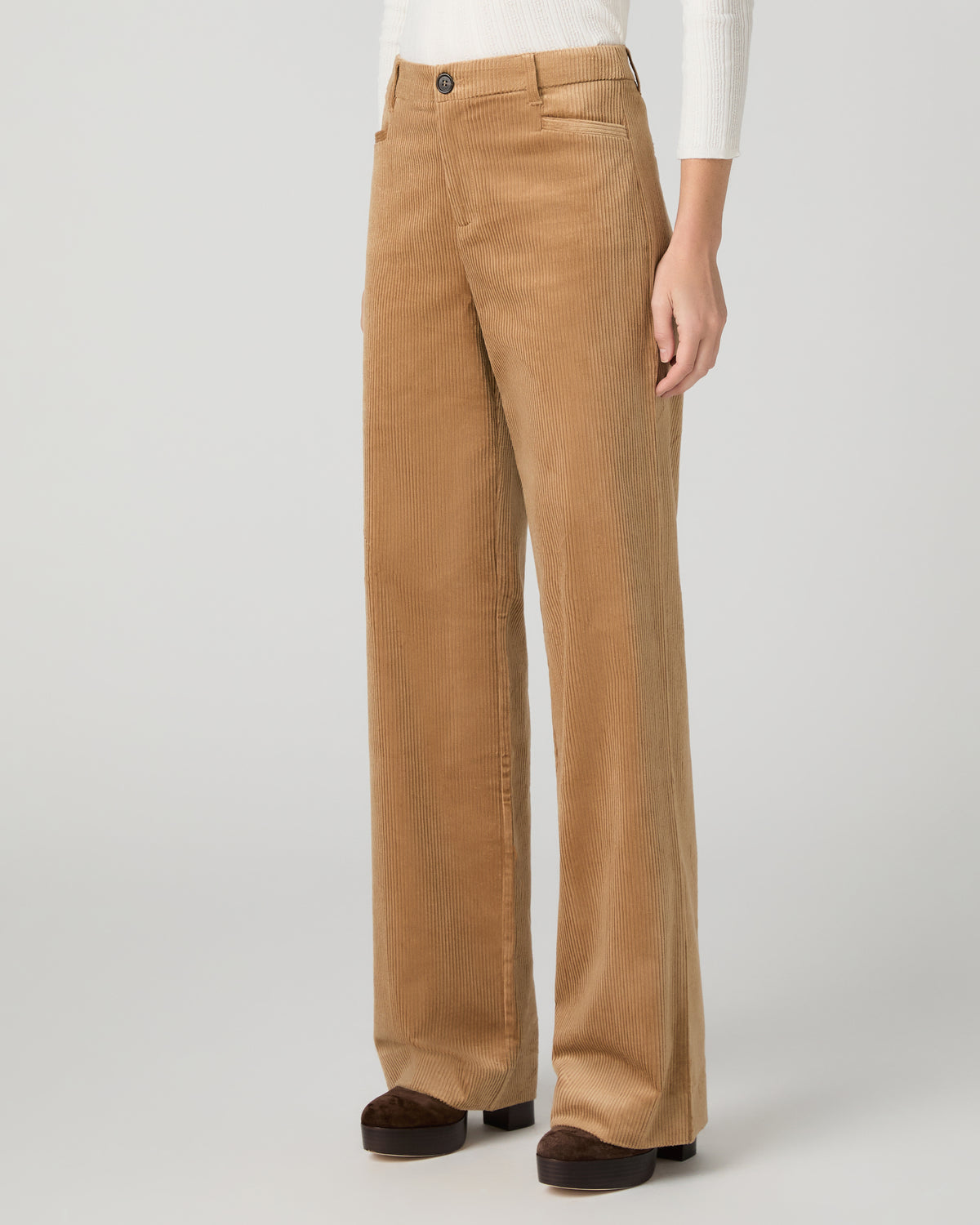 A woman modeling a white long-sleeve knit top with lace trim and tan wide-leg corduroy pants against a light gray studio background.