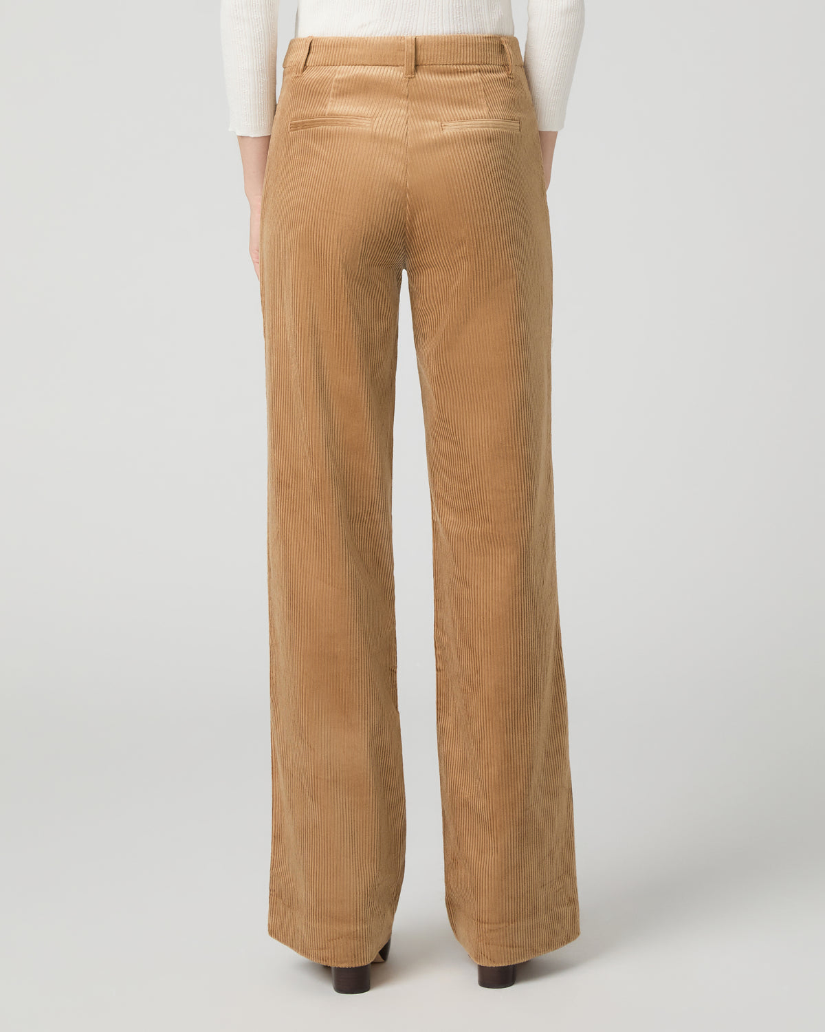 A woman modeling a white long-sleeve knit top with lace trim and tan wide-leg corduroy pants against a light gray studio background.