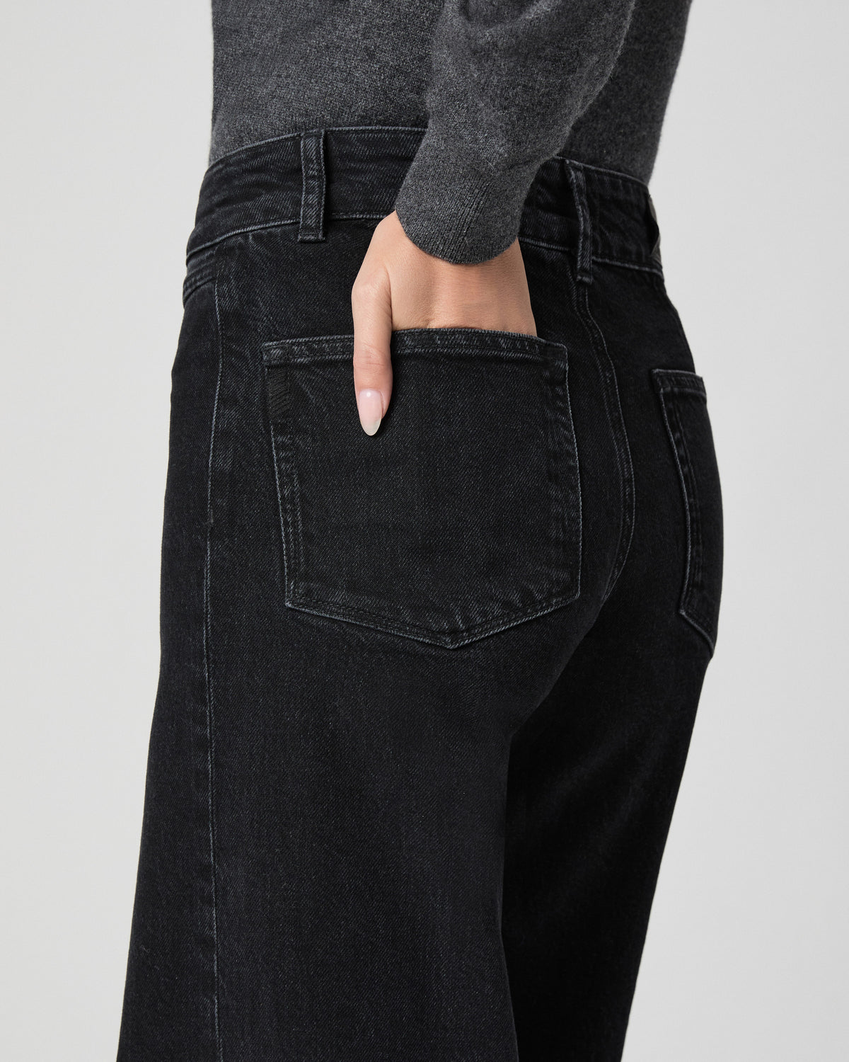 Close-up of the back pocket of the Sasha Wide Leg Jean in Downtown Noir black; model has one hand in the pocket and wears a grey top