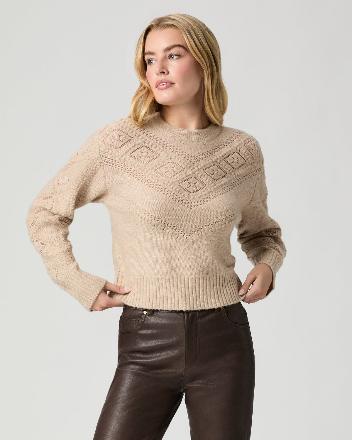 Model standing with hands on her hips, wearing the Sutter Sweater in Oatmeal Heather with dark brown coated jeans