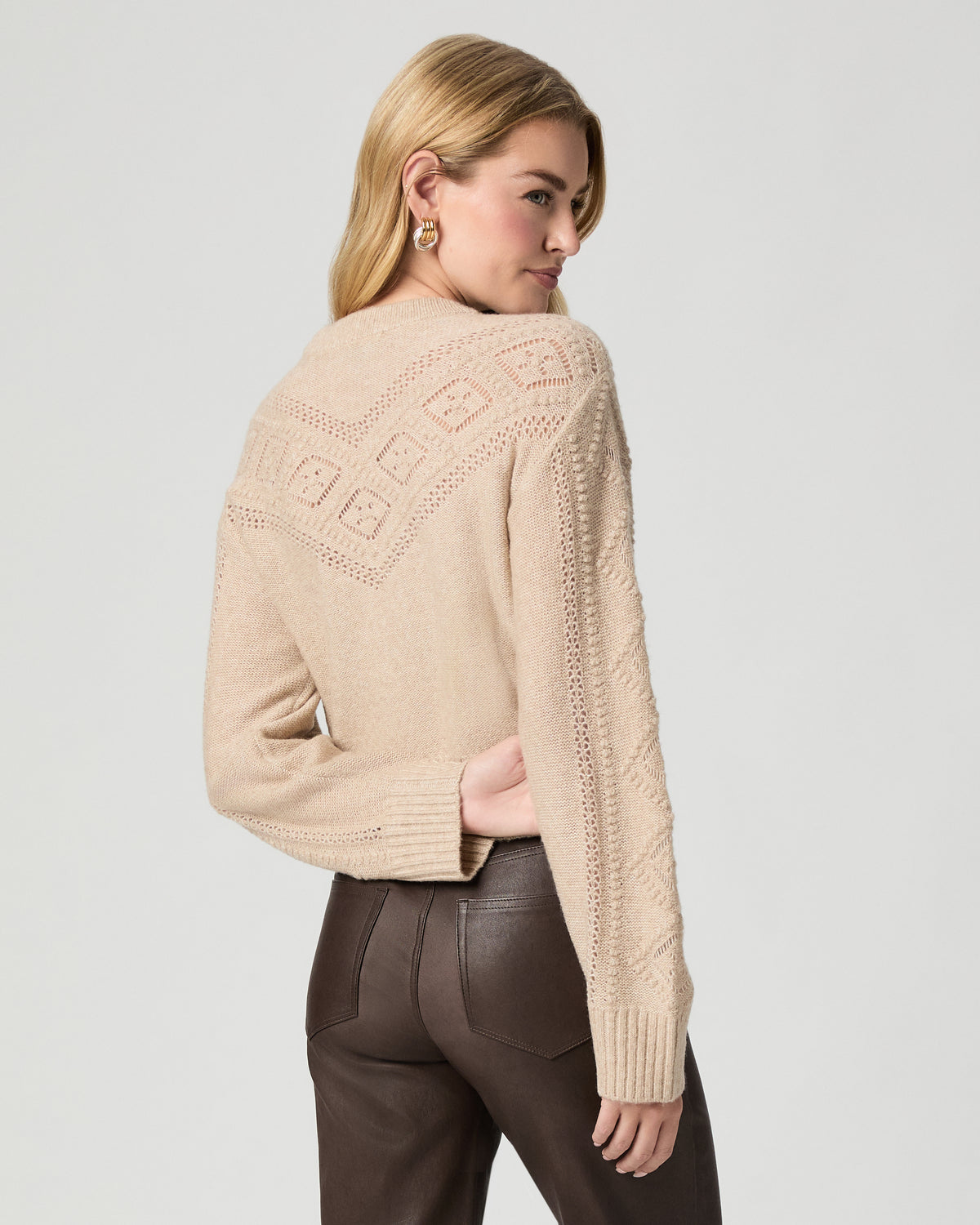 Back view of model looking over her shoulder, wearing the Sutter Sweater in Oatmeal Heather with dark brown coated jeans