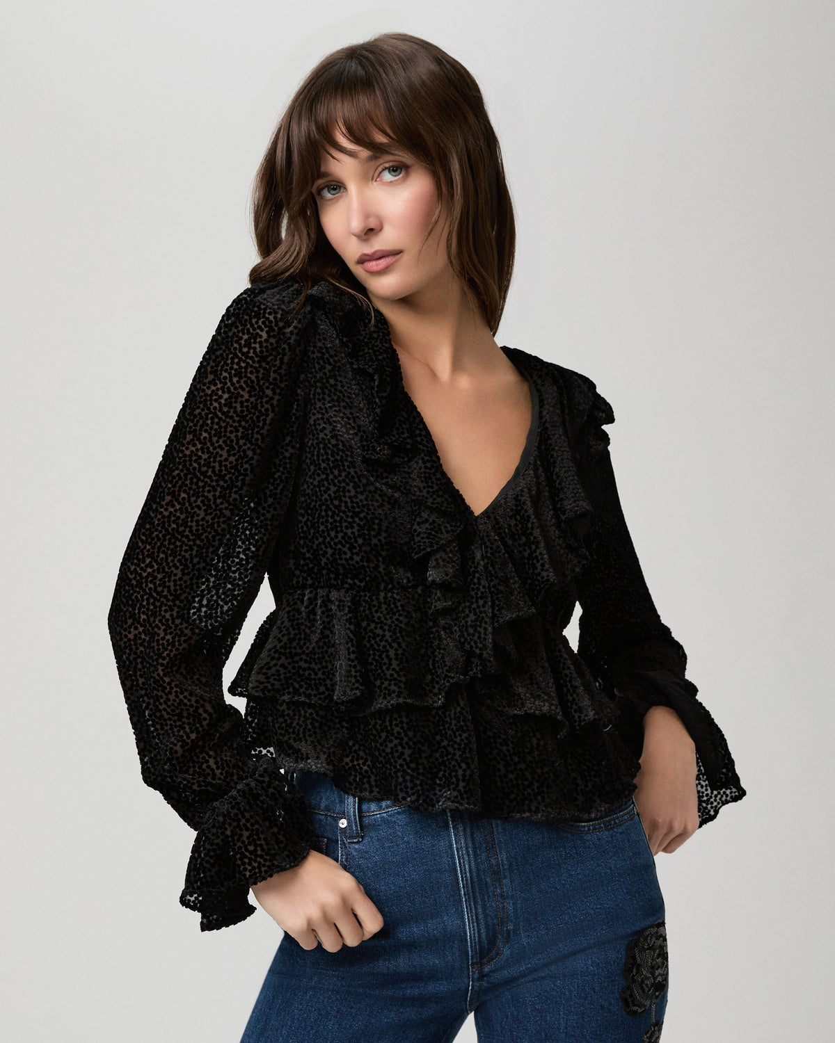 Close-up of the Aurelie Blouse in black mini-dot velvet burnout with a ruffled V-neckline and ruffle cuffs, worn with jeans