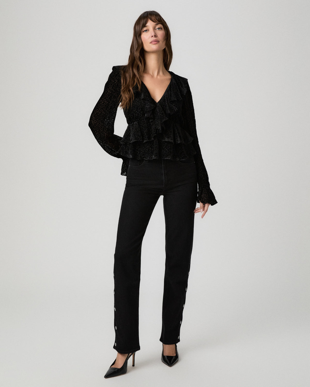 Full-length view of the black Aurelie Blouse with a ruffled peplum hem, styled with black straight-leg pants and heels