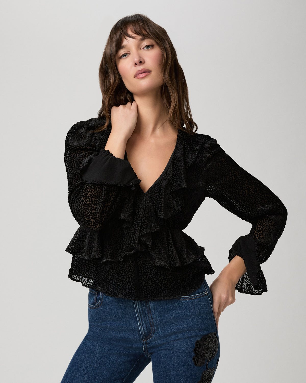 Model posing in the Aurelie Blouse in sheer black dot velvet with tiered ruffles and flared cuffs