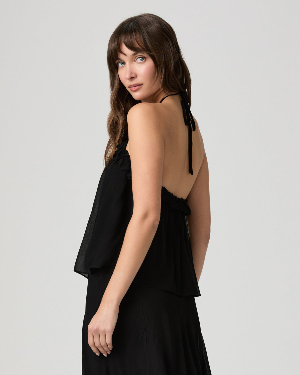 Back view of the Noor Top in black showing the open halter back and draped silhouette
