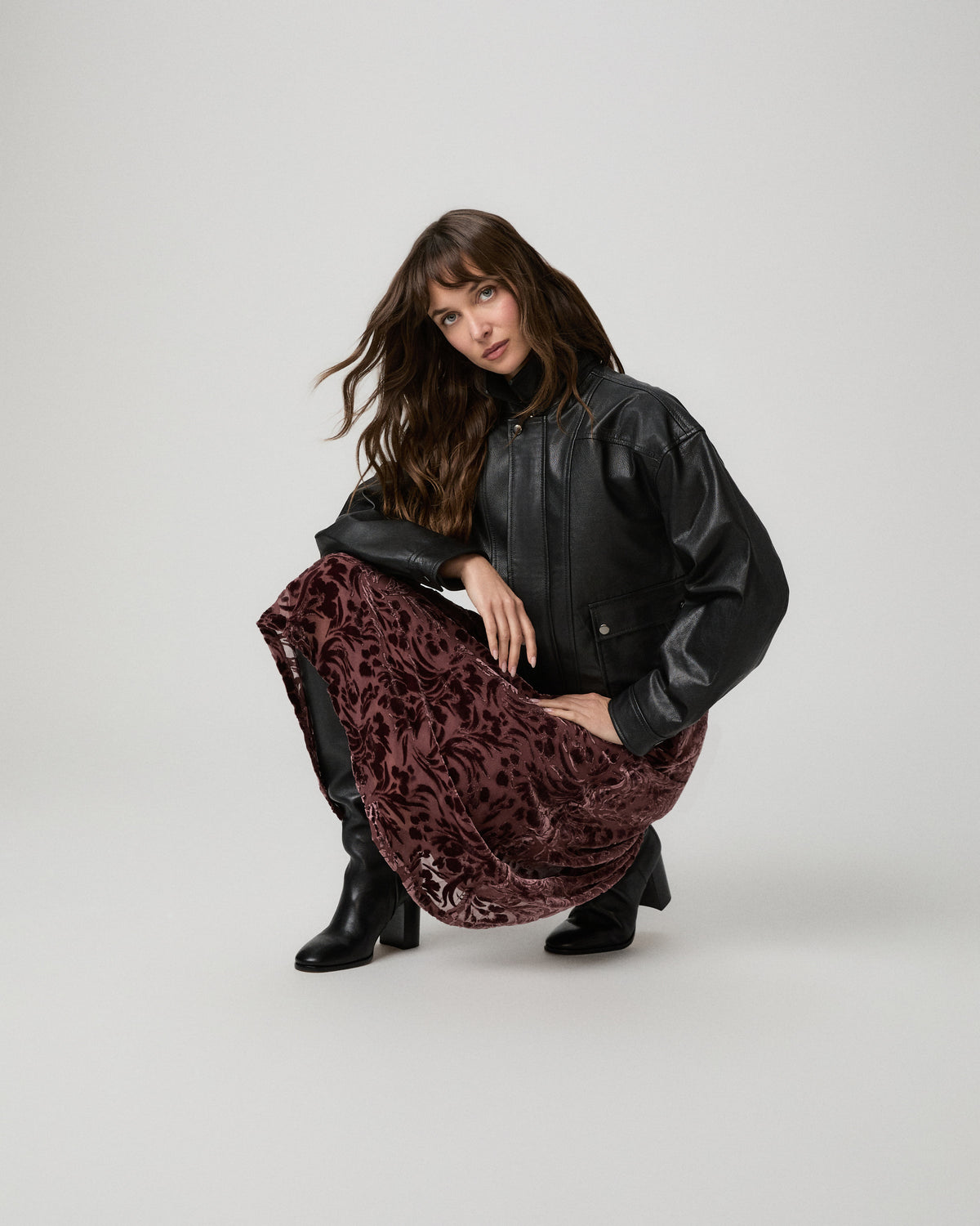 Model crouching in the merlot velvet burnout Rylie Skirt and a black leather jacket