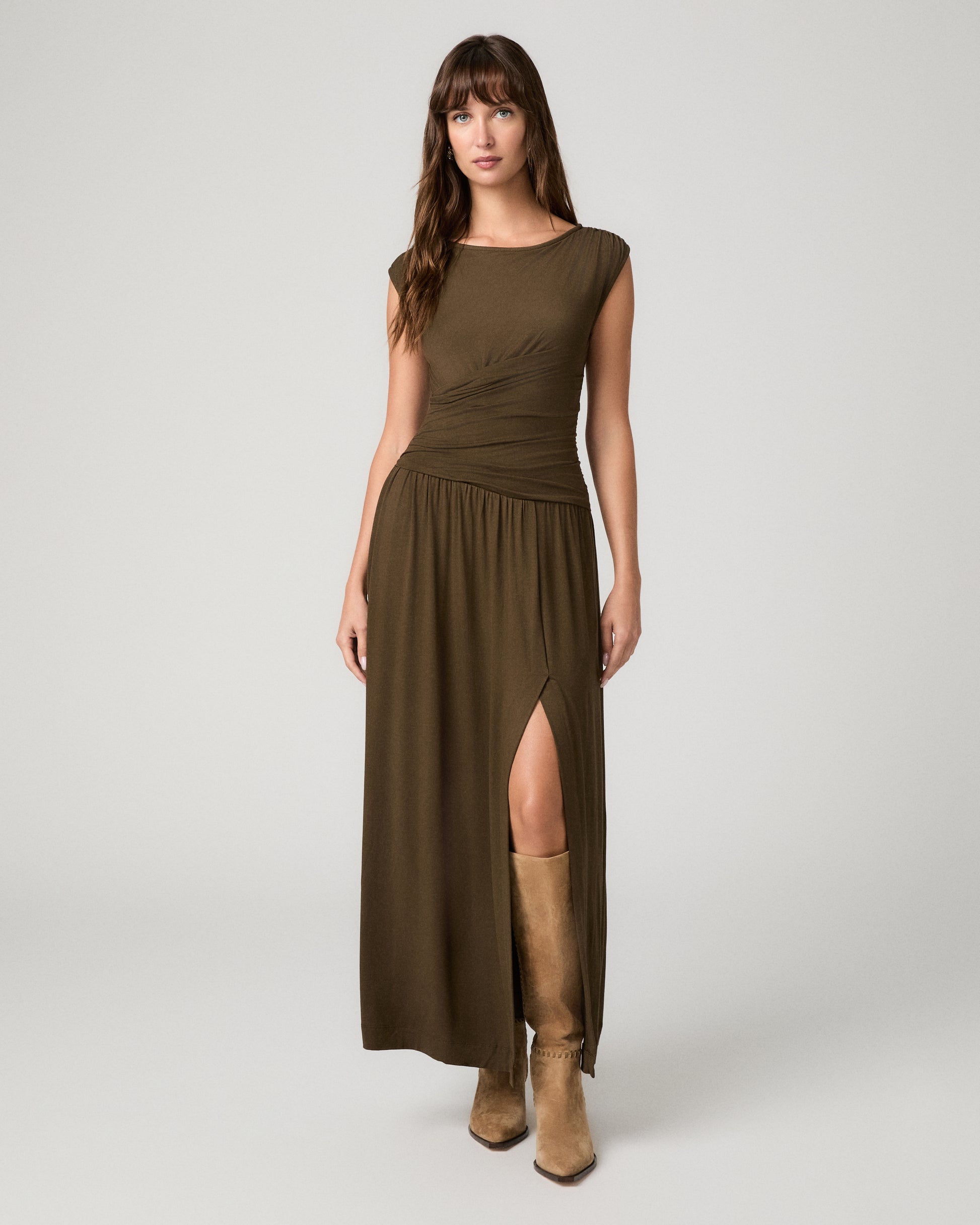 Women wearing a dark green maxi dress paired with brown boots against a white background