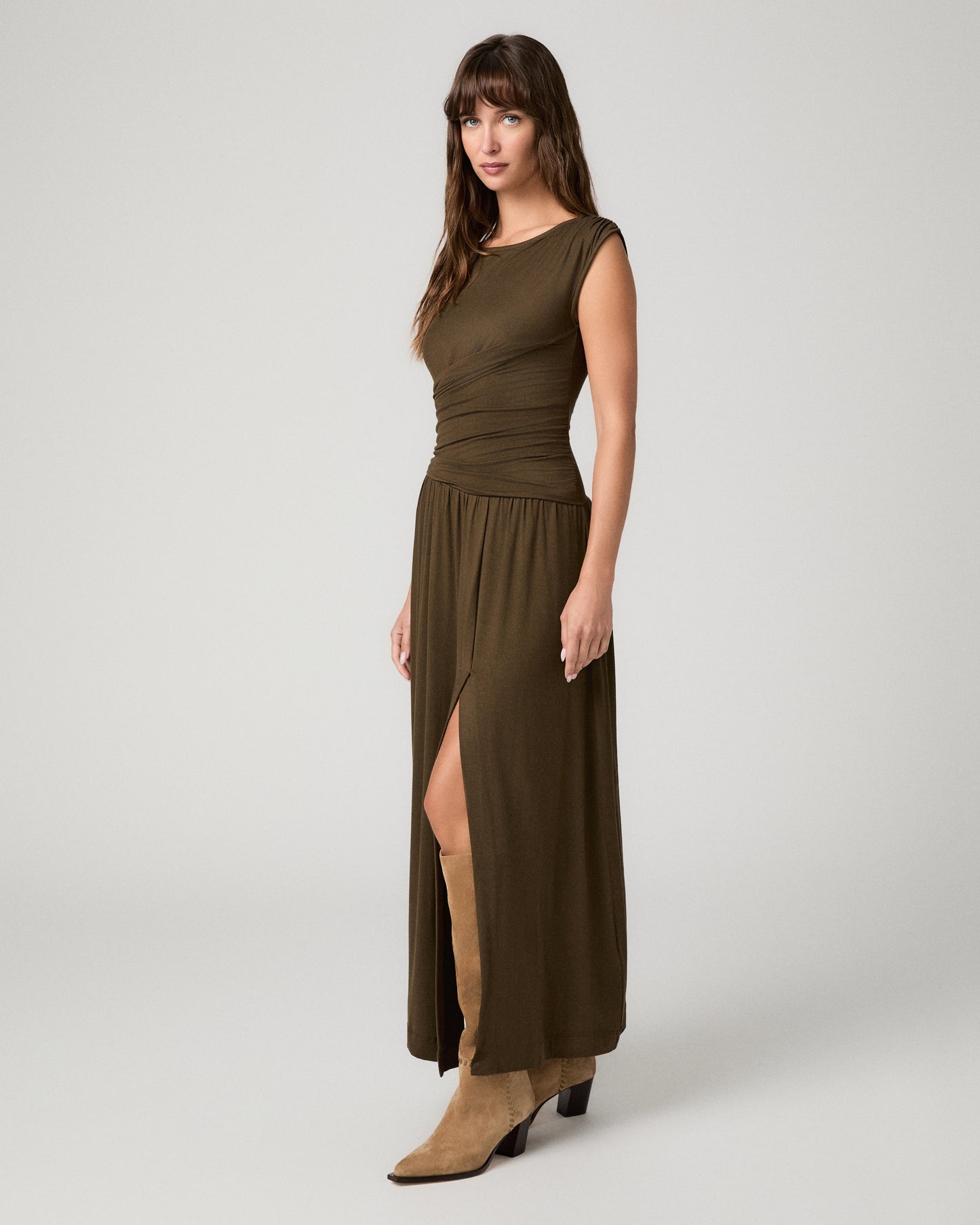 Women wearing a dark green maxi dress paired with brown boots against a white background