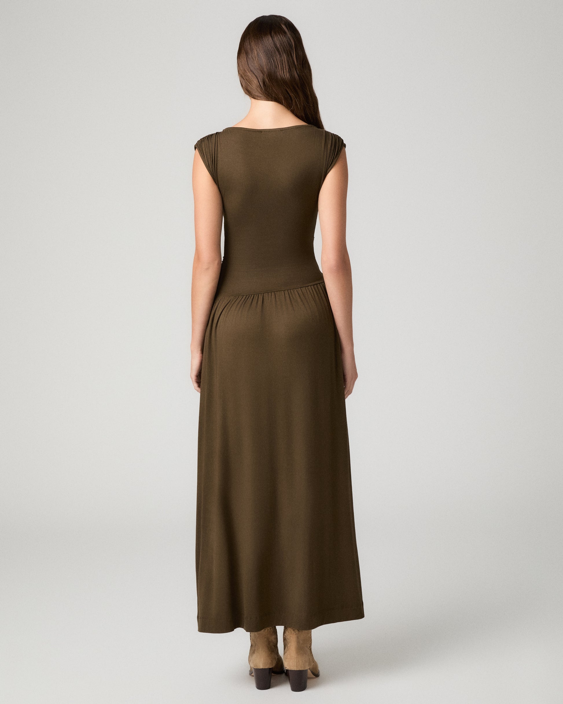 Women wearing a dark green maxi dress paired with brown boots against a white background