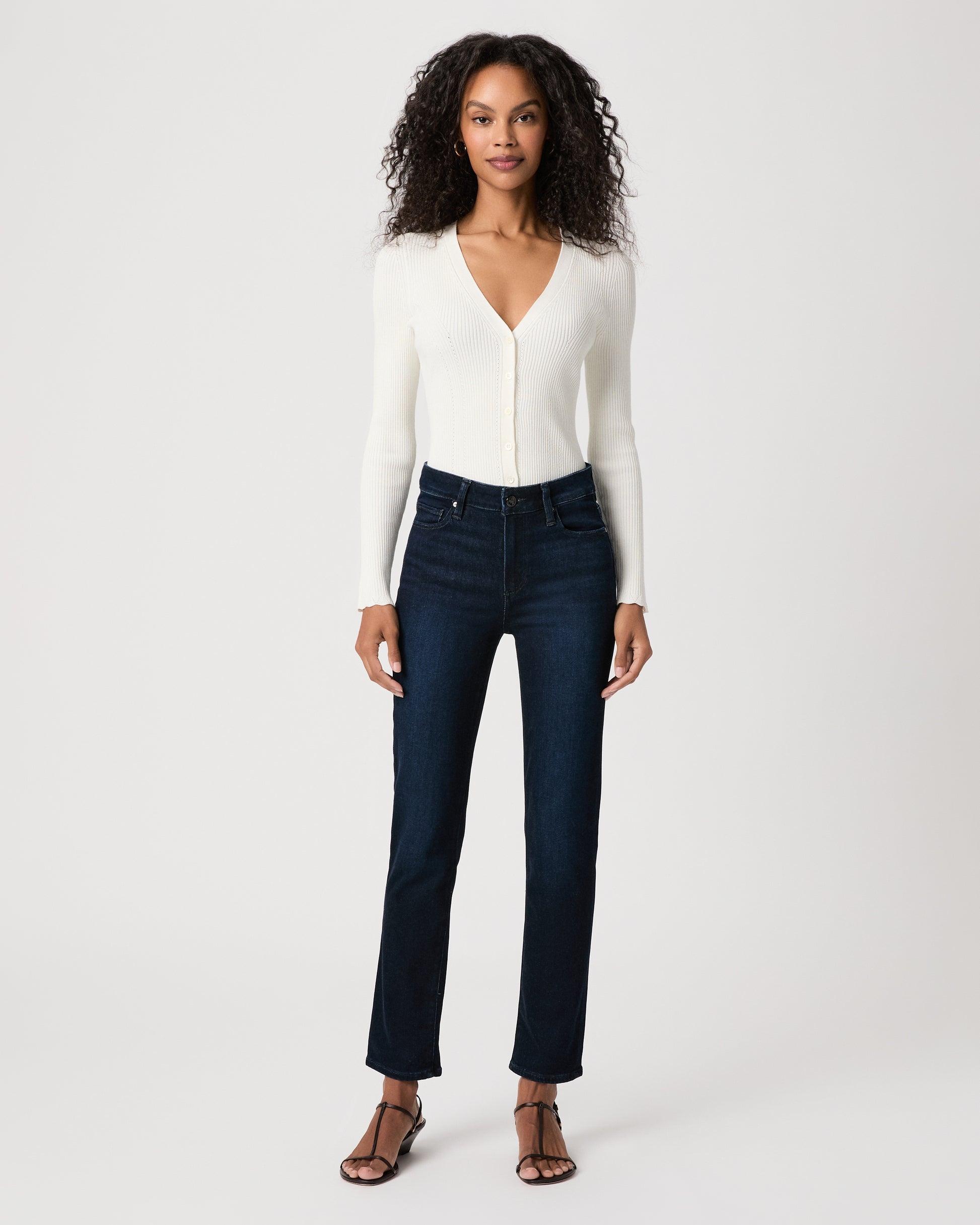 women wearing a white top paired with dark blue jeans and black sandals against a white background 