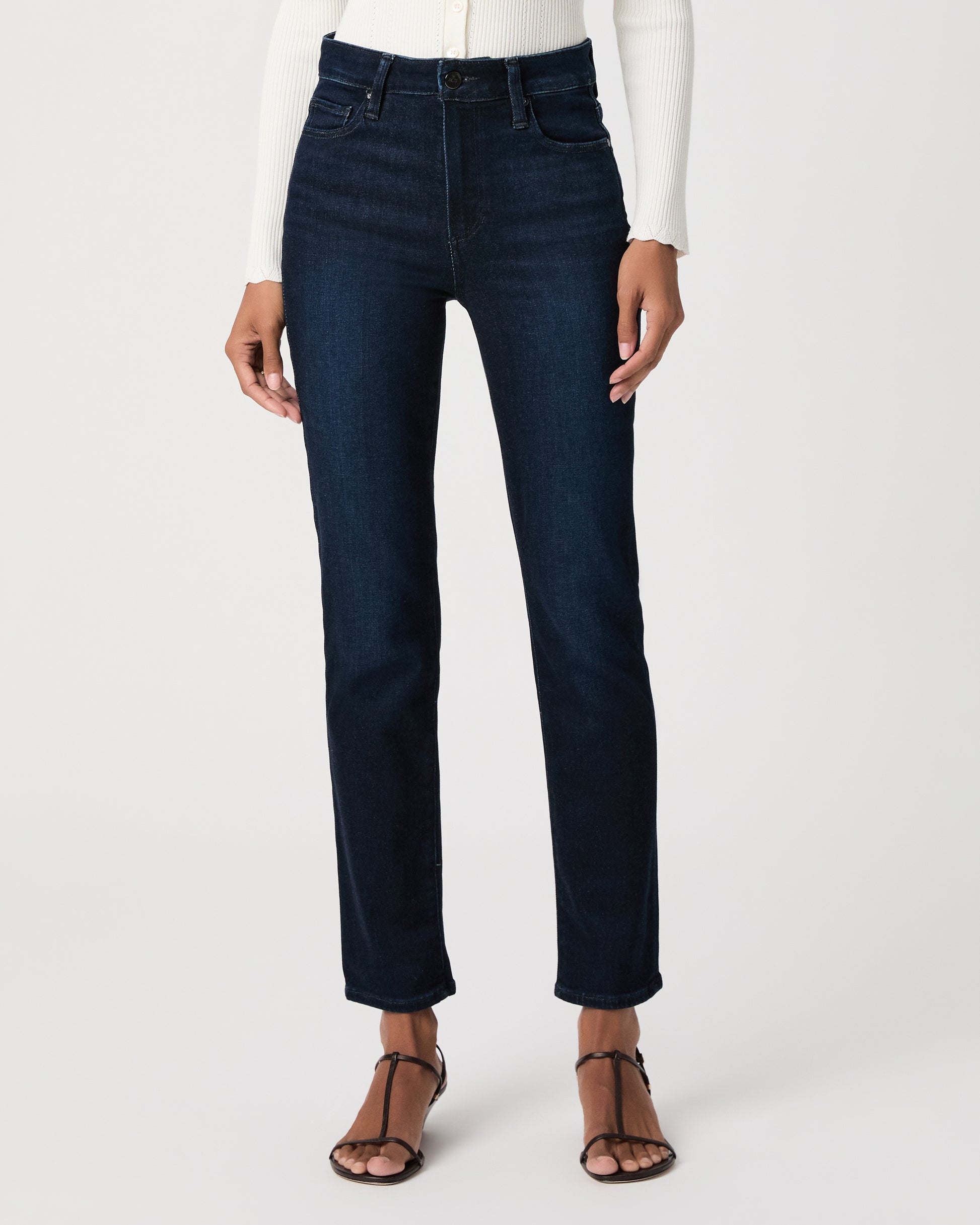 women wearing a white top paired with dark blue jeans and black sandals against a white background 