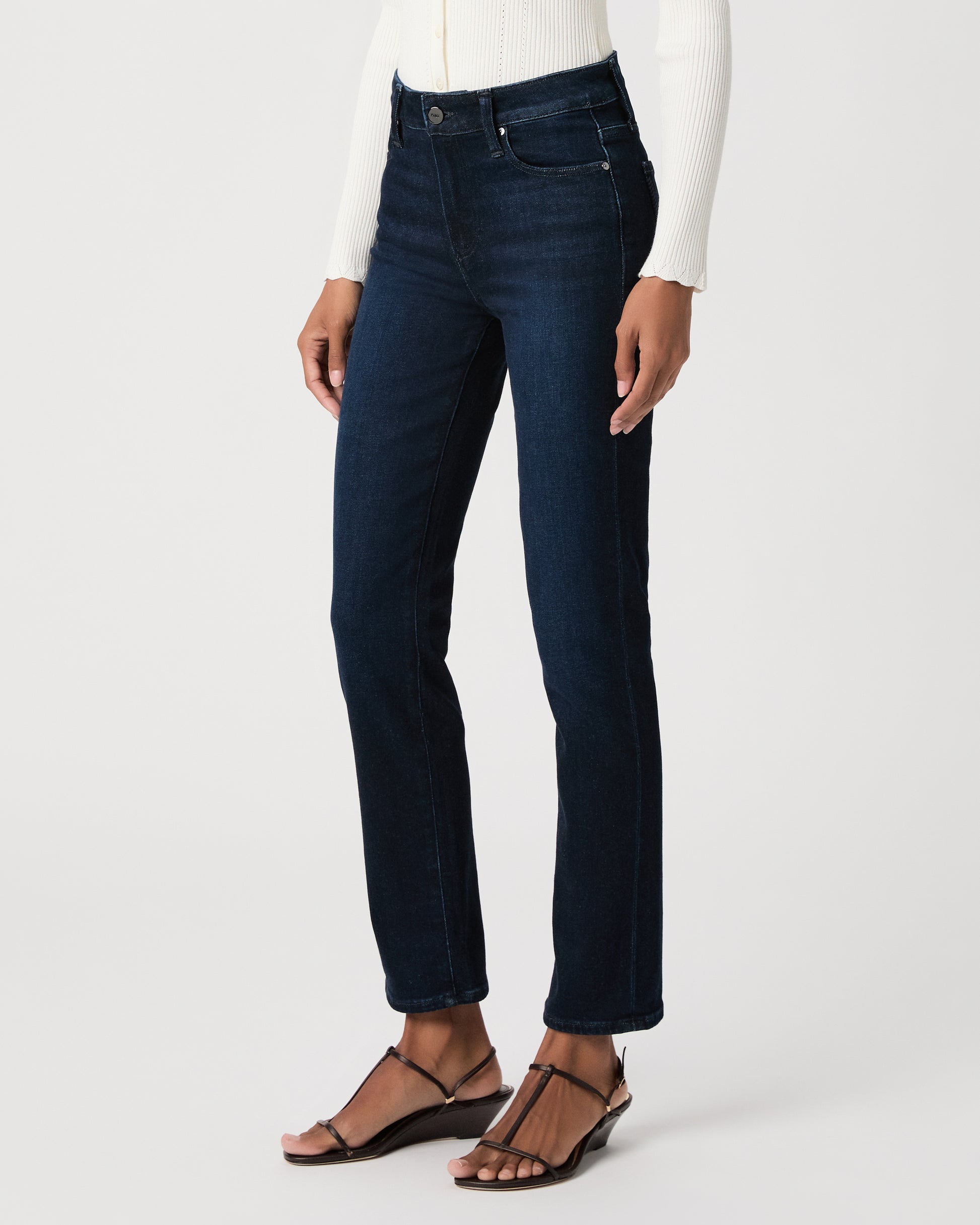 women wearing a white top paired with dark blue jeans and black sandals against a white background 