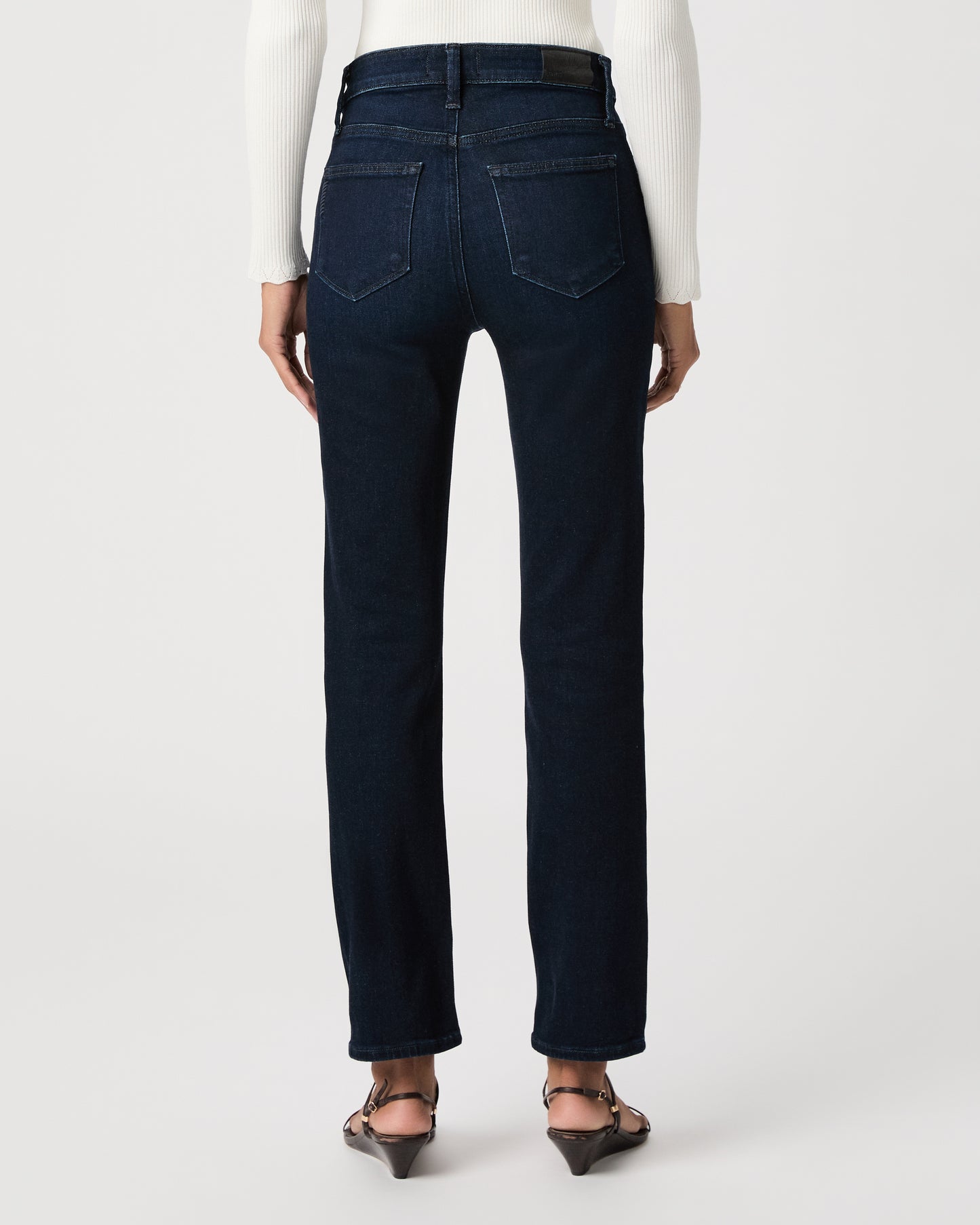 women wearing a white top paired with dark blue jeans and black sandals against a white background 