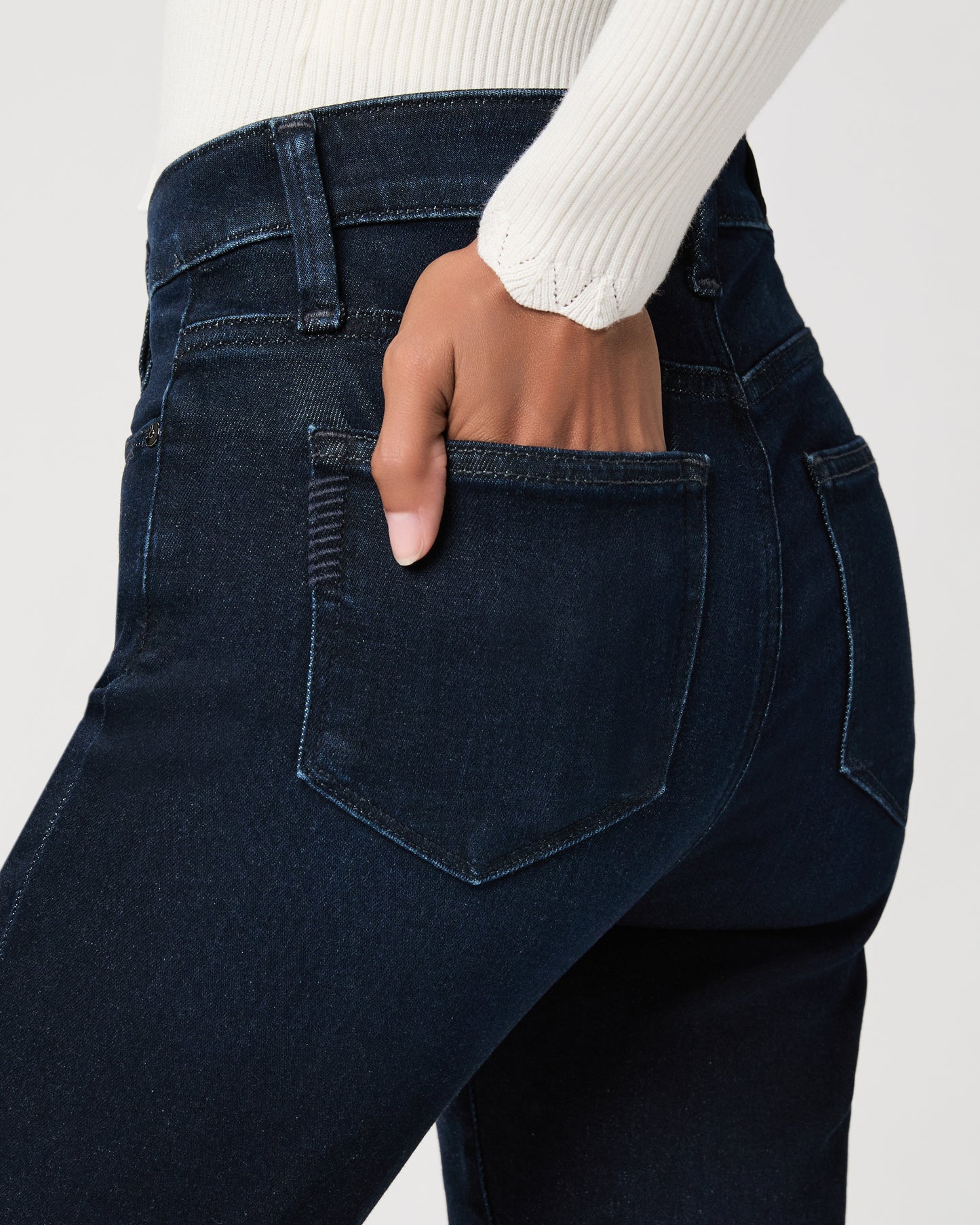 women wearing a white top paired with dark blue jeans and black sandals against a white background 