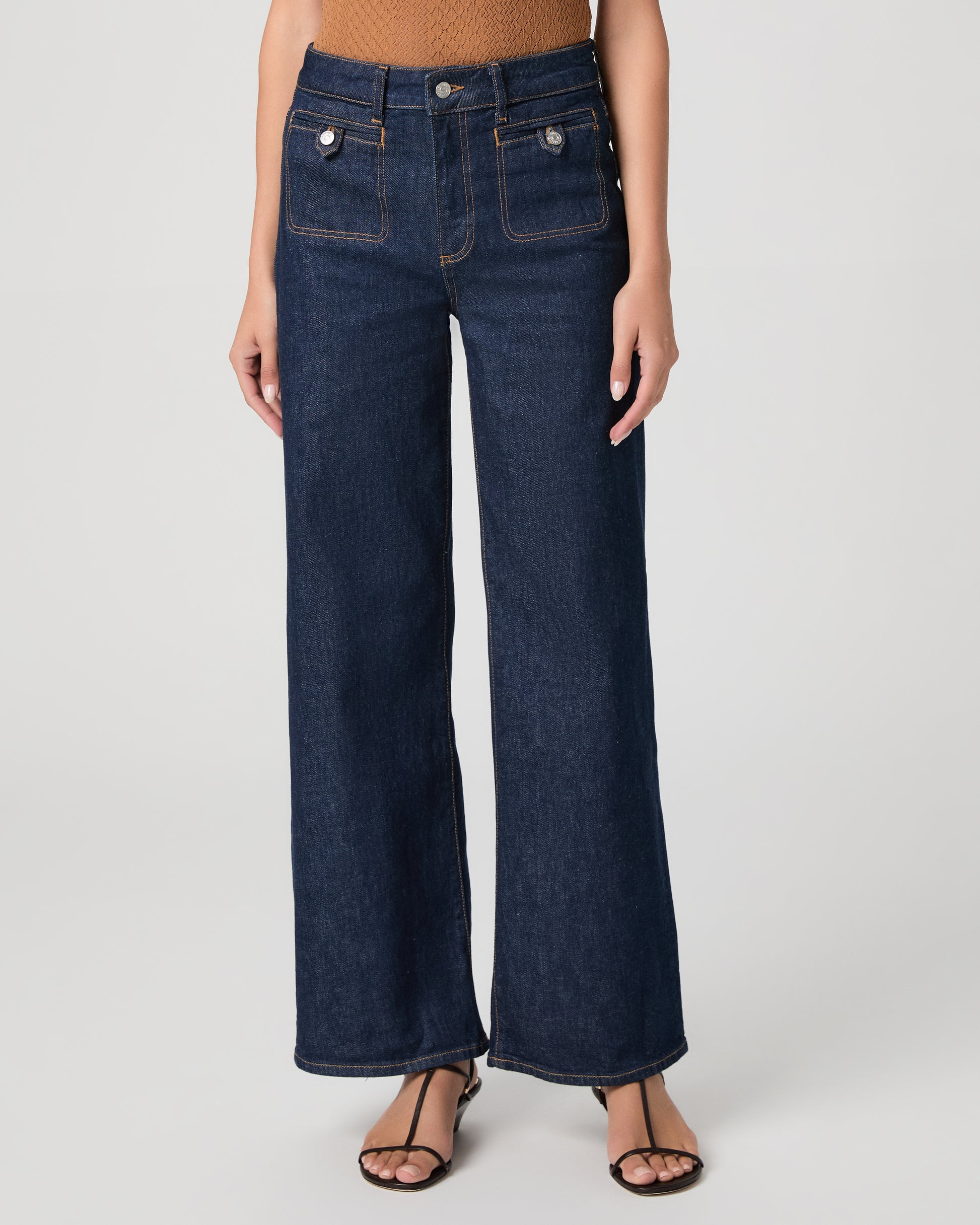 Woman wearing a brown top and blue jeans on a white background