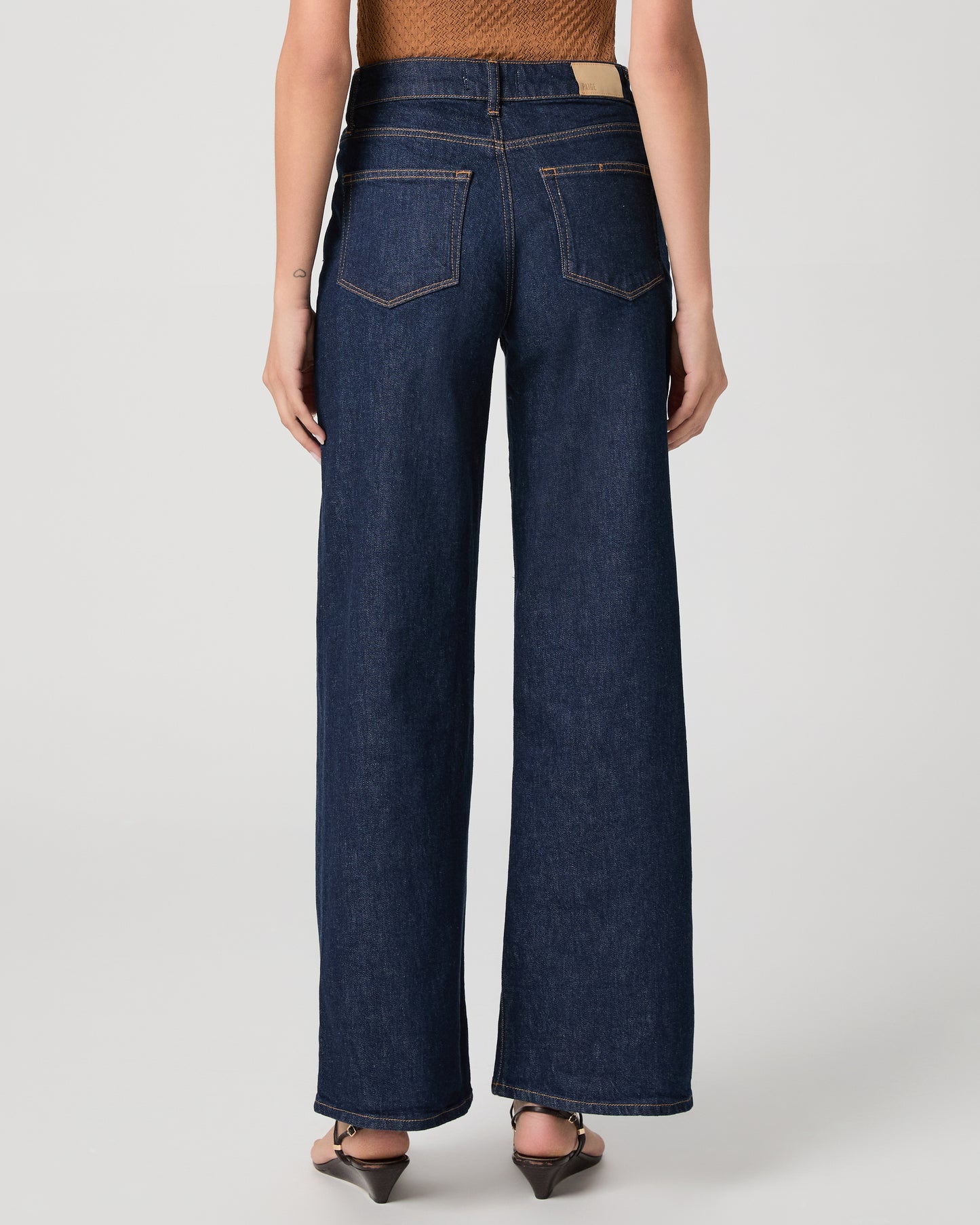 Woman wearing a brown top and blue jeans on a white background