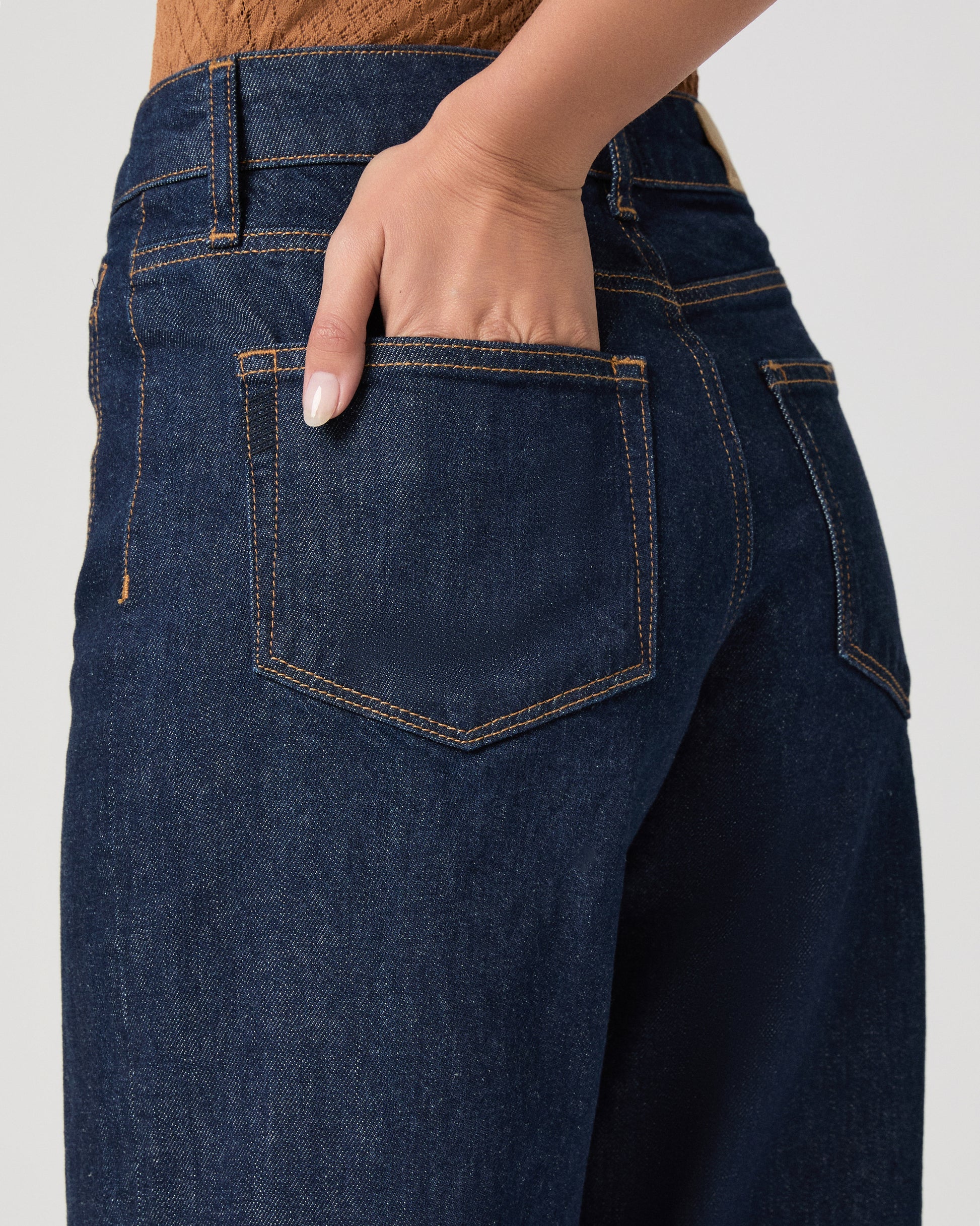 Woman wearing a brown top and blue jeans on a white background