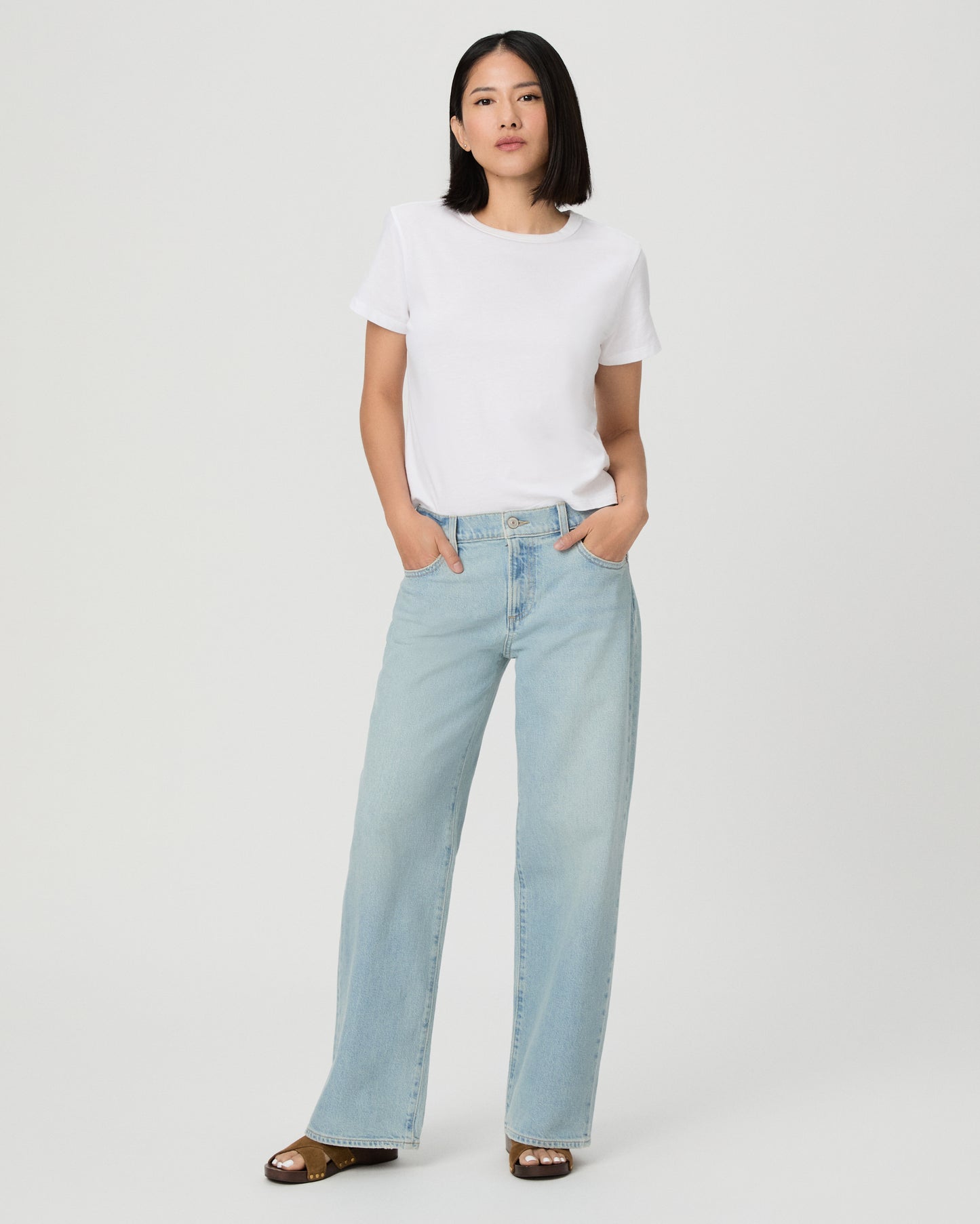 A model wearing a white short-sleeve t-shirt and light-wash wide-leg denim jeans, standing against a plain light gray studio background.