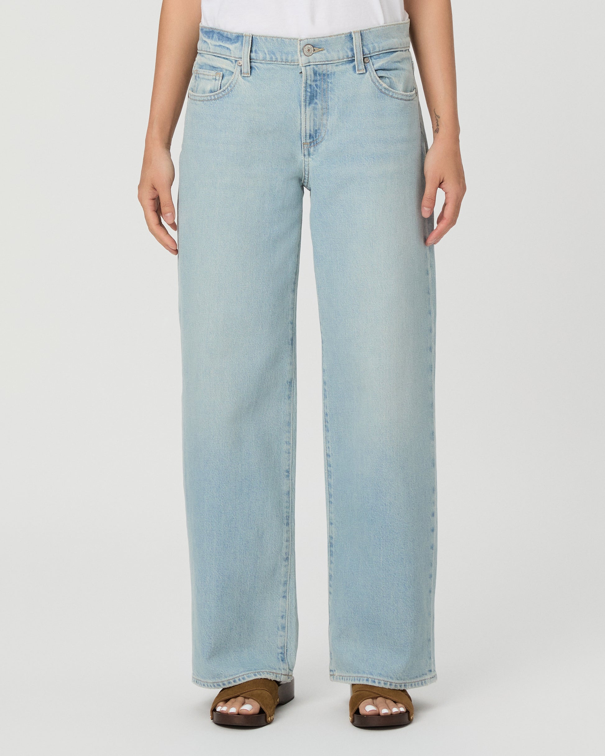 A model wearing a white short-sleeve t-shirt and light-wash wide-leg denim jeans, standing against a plain light gray studio background.