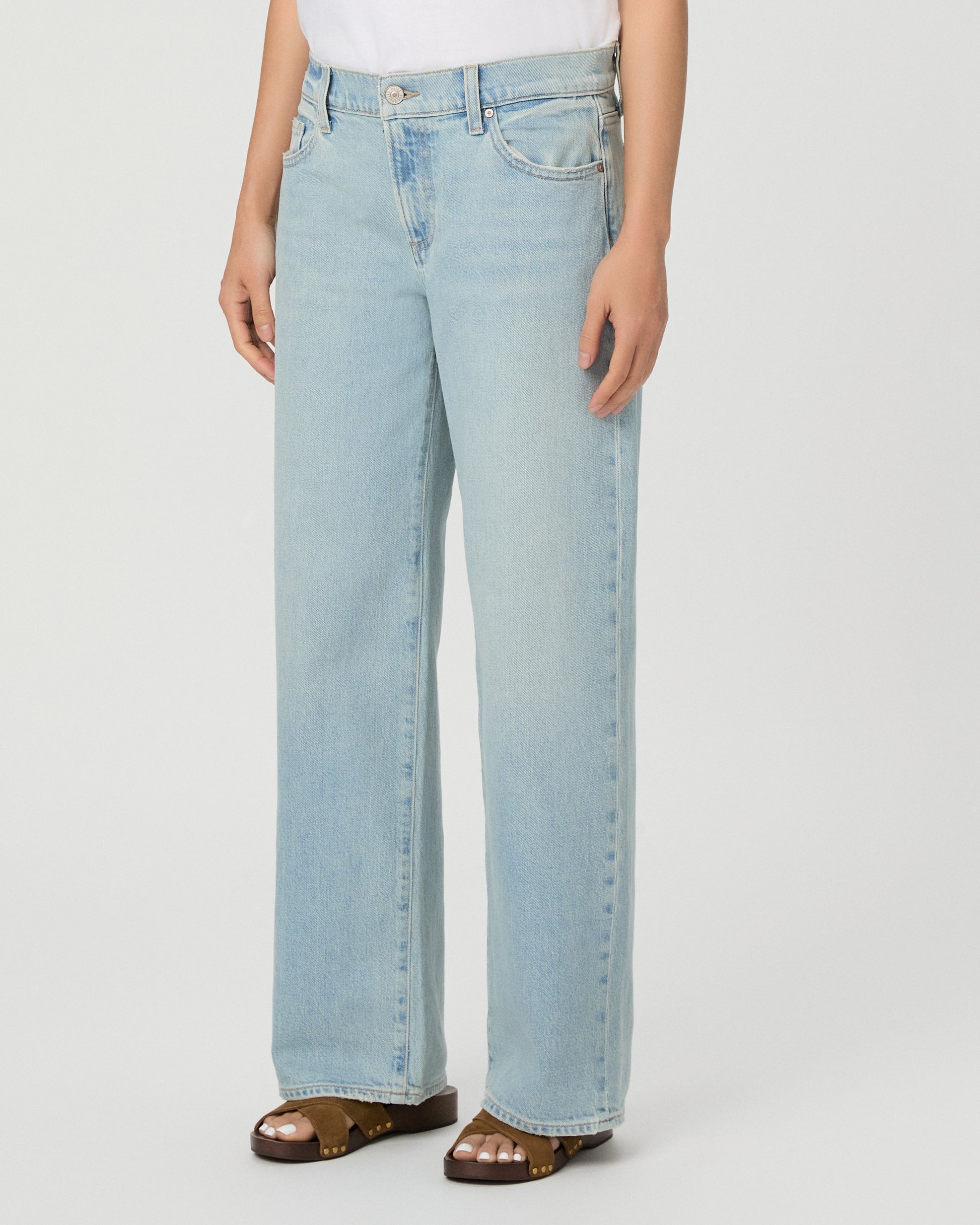 A model wearing a white short-sleeve t-shirt and light-wash wide-leg denim jeans, standing against a plain light gray studio background.