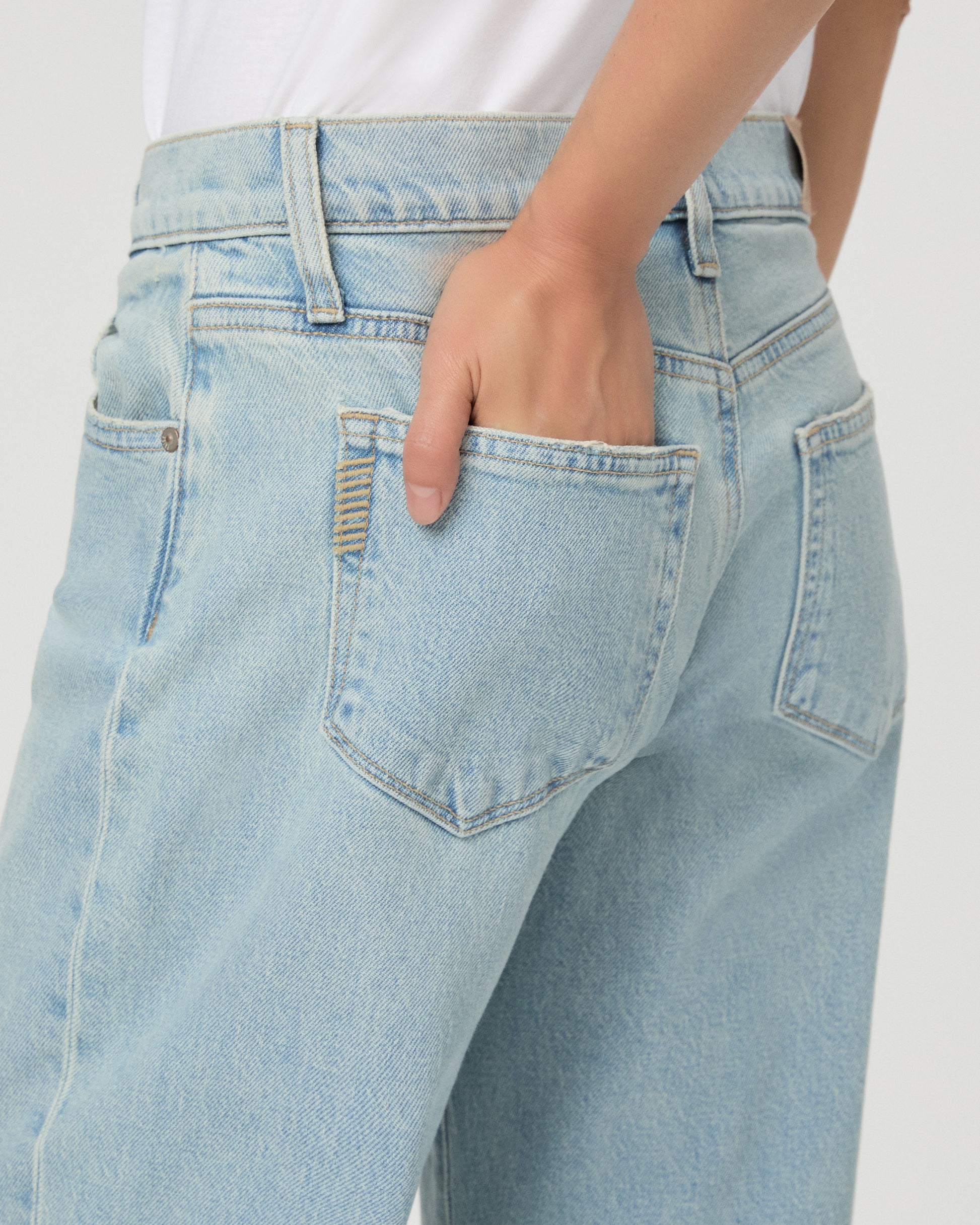 A model wearing a white short-sleeve t-shirt and light-wash wide-leg denim jeans, standing against a plain light gray studio background.