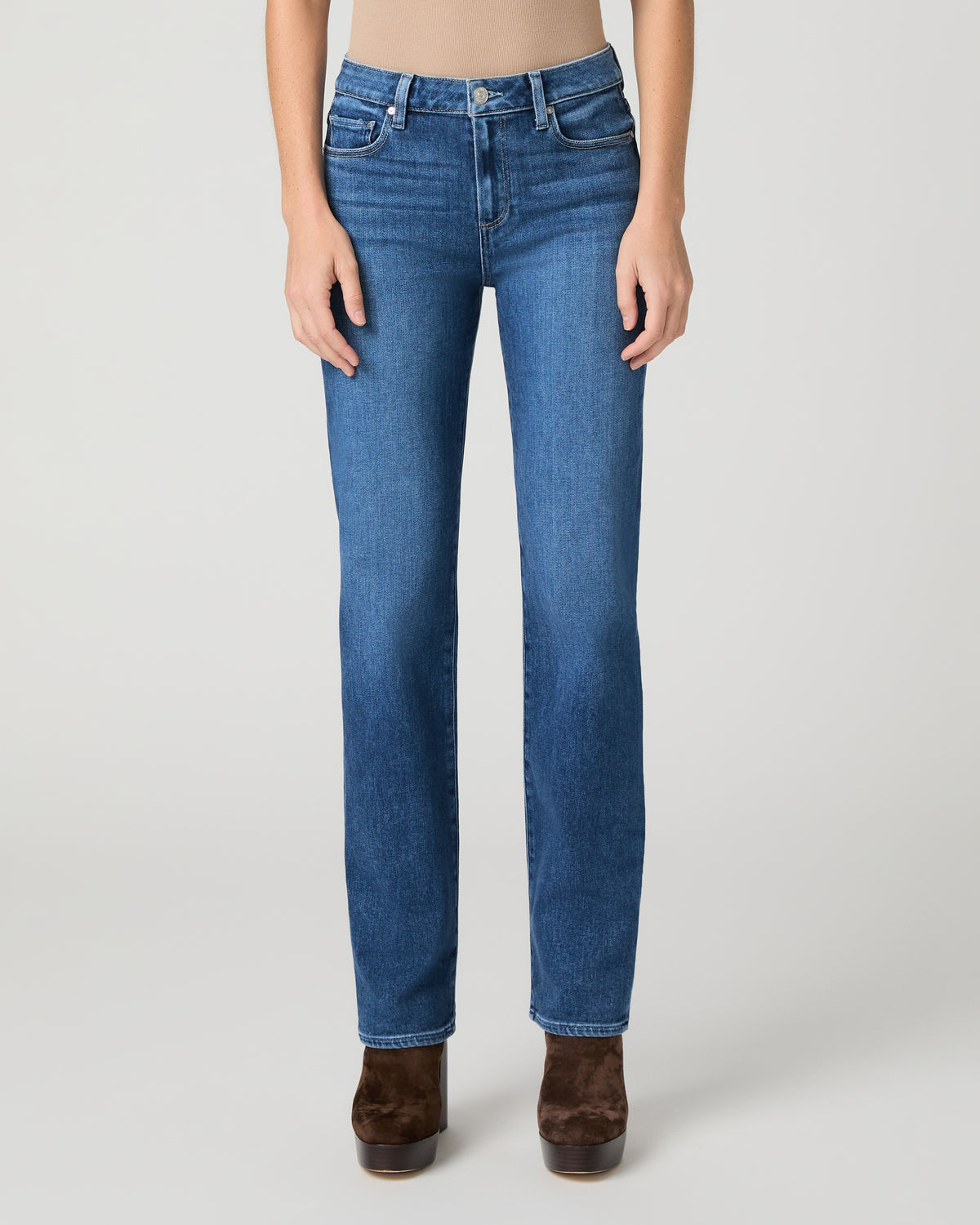 Women wearing brown top and blue jeans paired with brown boots against a white background