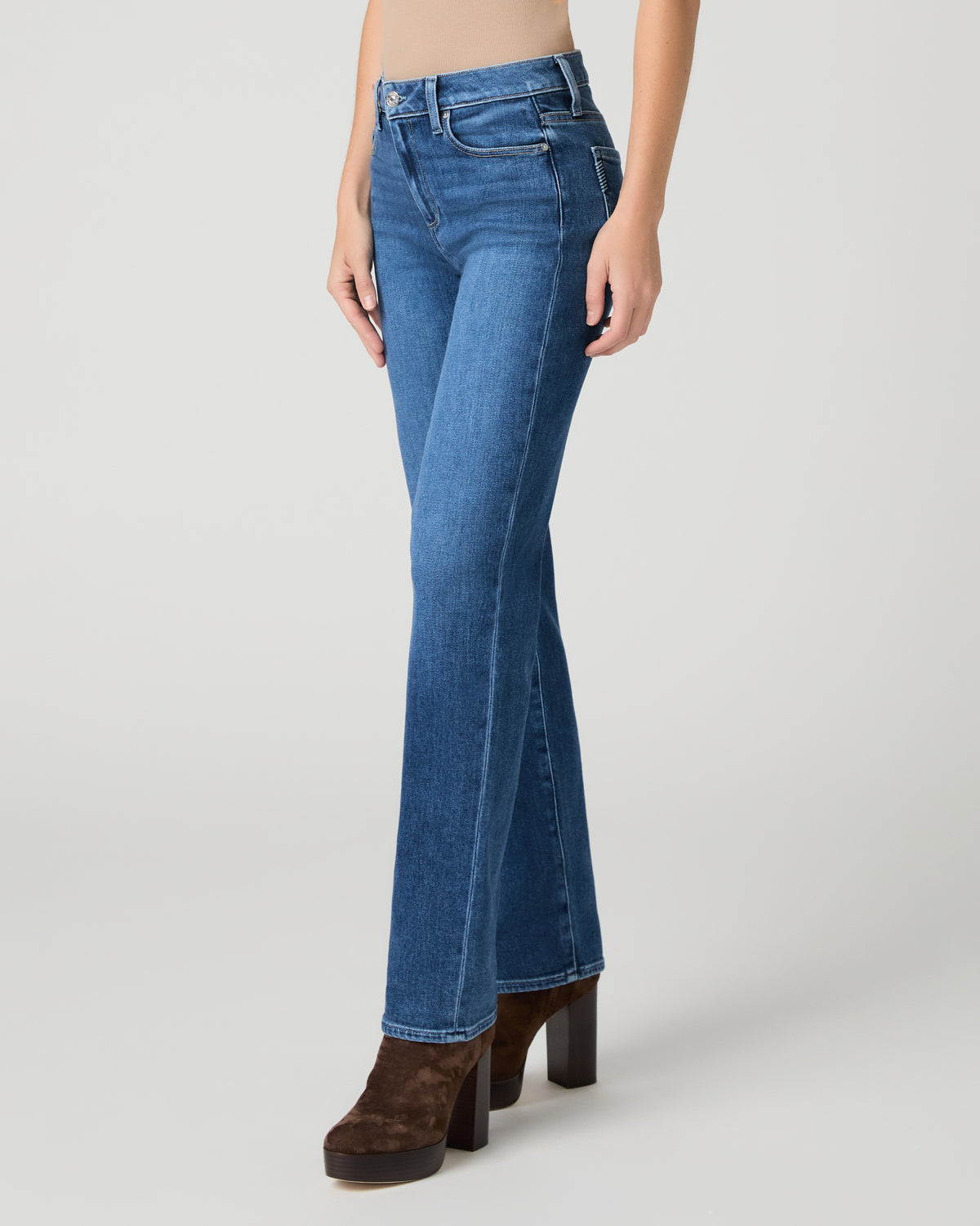 Women wearing brown top and blue jeans paired with brown boots against a white background