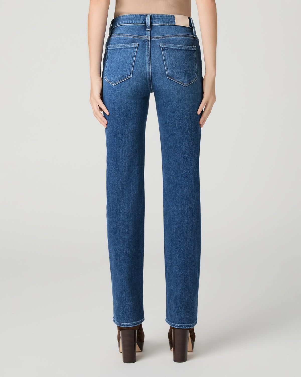 Women wearing brown top and blue jeans paired with brown boots against a white background