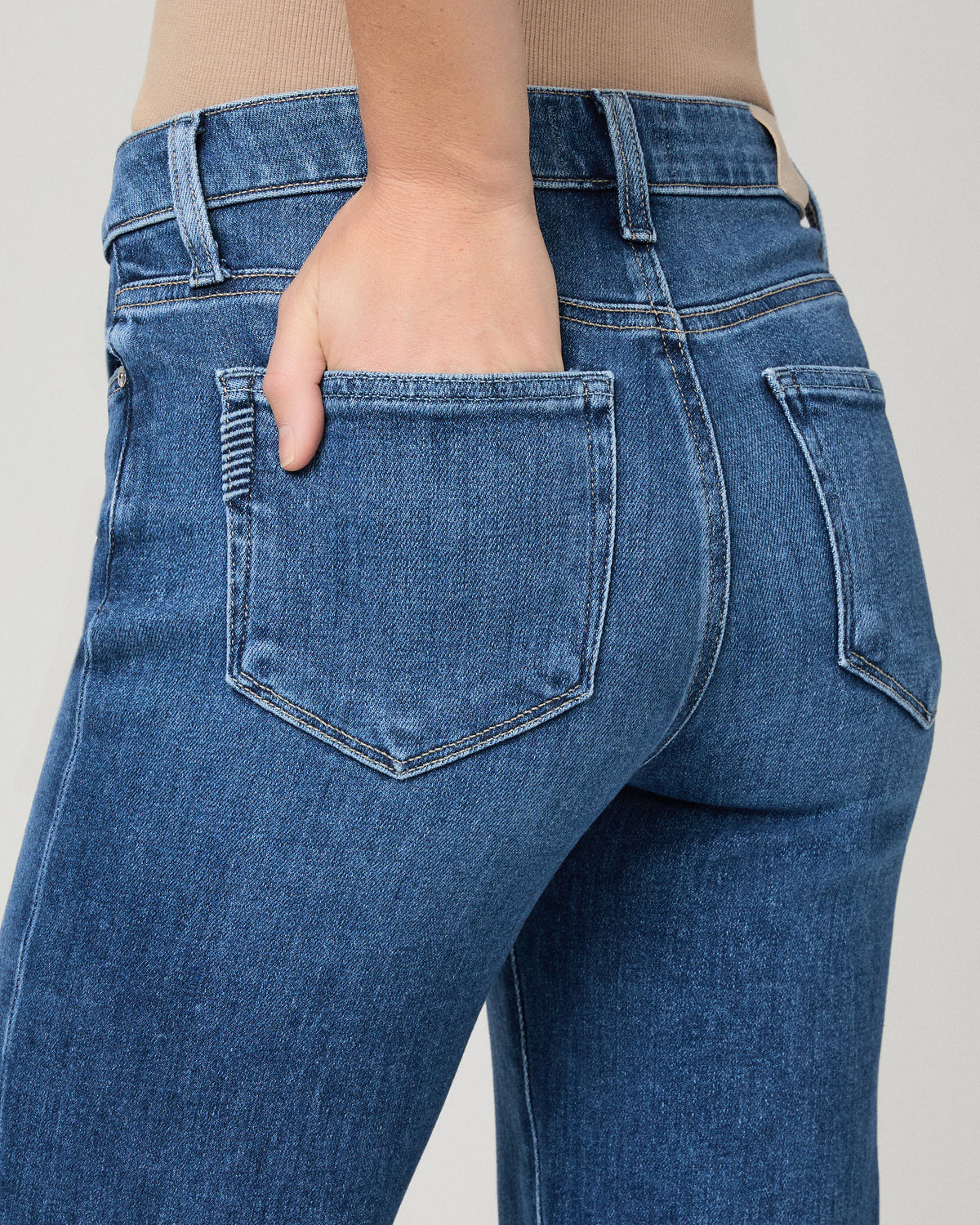 Women wearing brown top and blue jeans against a white background