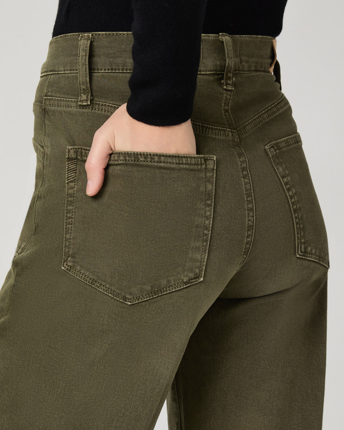Close-up of the olive green Arellia Skimmer Barrel Leg Jean's back pocket, with a hand tucked into the pocket.