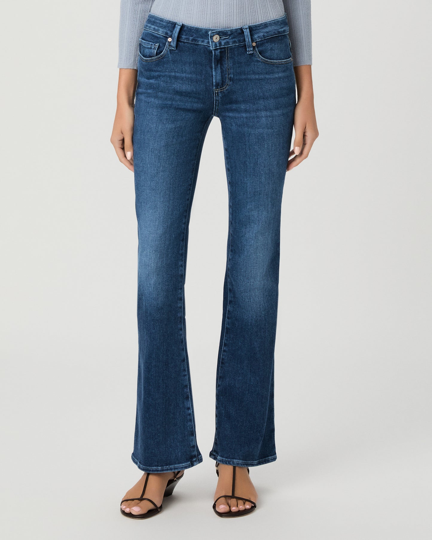 A woman modeling a light blue ribbed long-sleeve knit top with a buttoned henley neckline and dark blue flare jeans, standing against a light gray studio background.