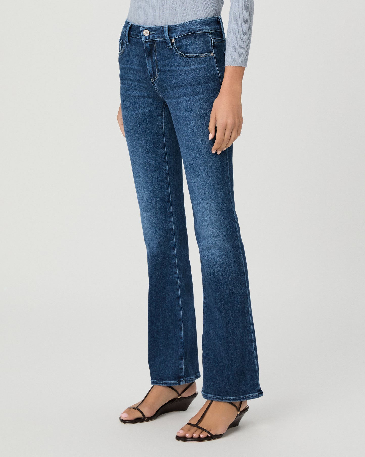 A woman modeling a light blue ribbed long-sleeve knit top with a buttoned henley neckline and dark blue flare jeans, standing against a light gray studio background.