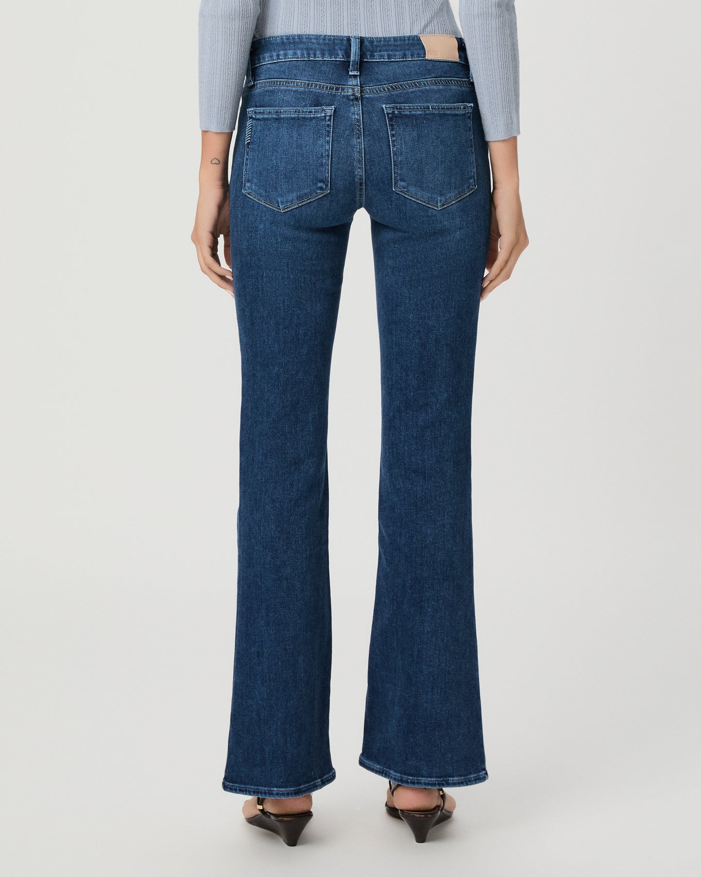 A woman modeling a light blue ribbed long-sleeve knit top with a buttoned henley neckline and dark blue flare jeans, standing against a light gray studio background.