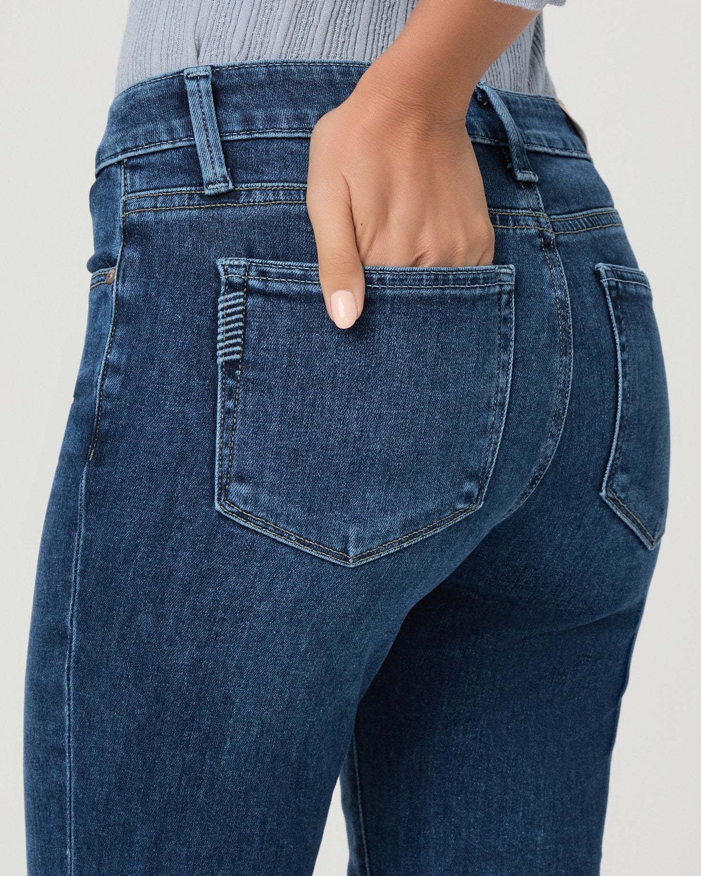 A woman modeling a light blue ribbed long-sleeve knit top with a buttoned henley neckline and dark blue flare jeans, standing against a light gray studio background.