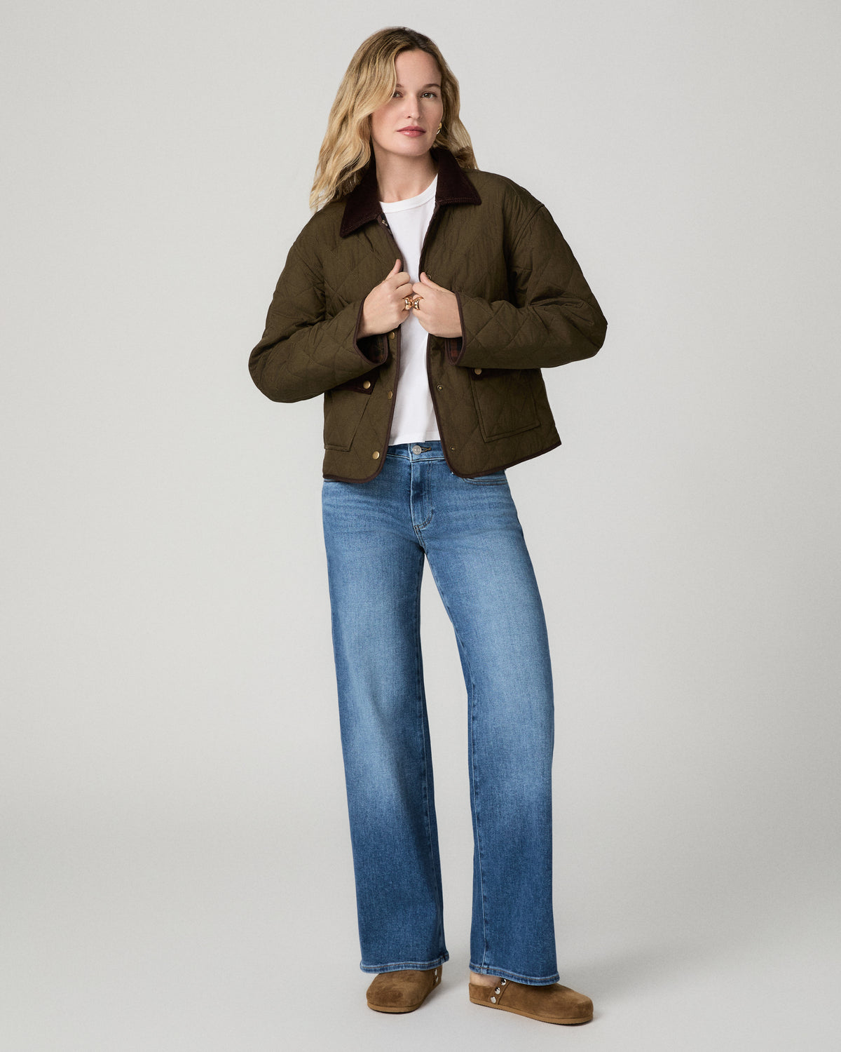 Women wearing a white tee paired with blue jeans and a green jacket standing against a white background